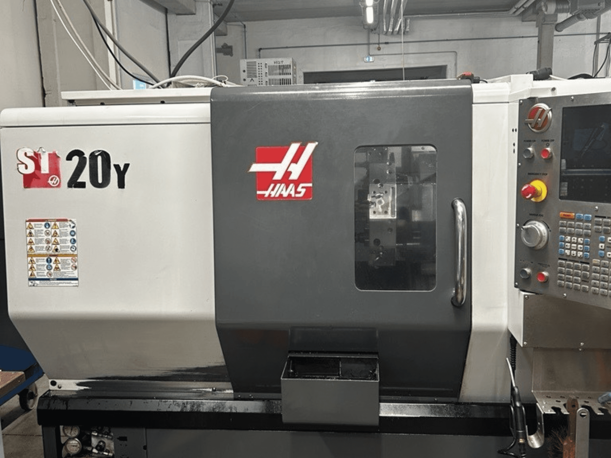 Haas ST-20Y CNC tekinimo staklės, priekinis vaizdas, kuriame matomas valdymo skydelis, saugos etiketės ir darbo langas.