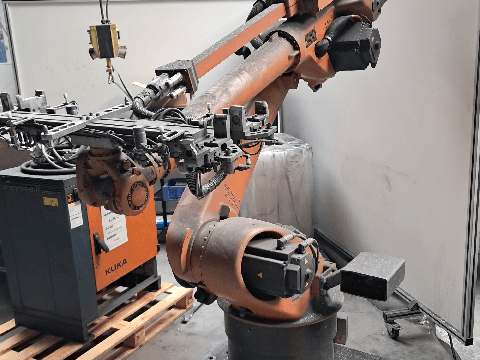 KUKA KR 30L16-2 roboto ranka, matoma iš šono, su sudėtingu galiniu įtaisu ir valdymo kabeliais, pastatyta šalia KUKA valdymo spintelės.