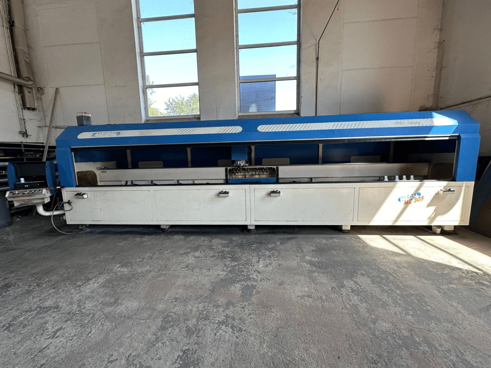 MECAL MC 305 vertikaliojo apdirbimo centro, pasižyminčio mėlynai baltu dizainu, matomu darbo stalu ir valdymo skydeliu, vaizdas iš priekio.