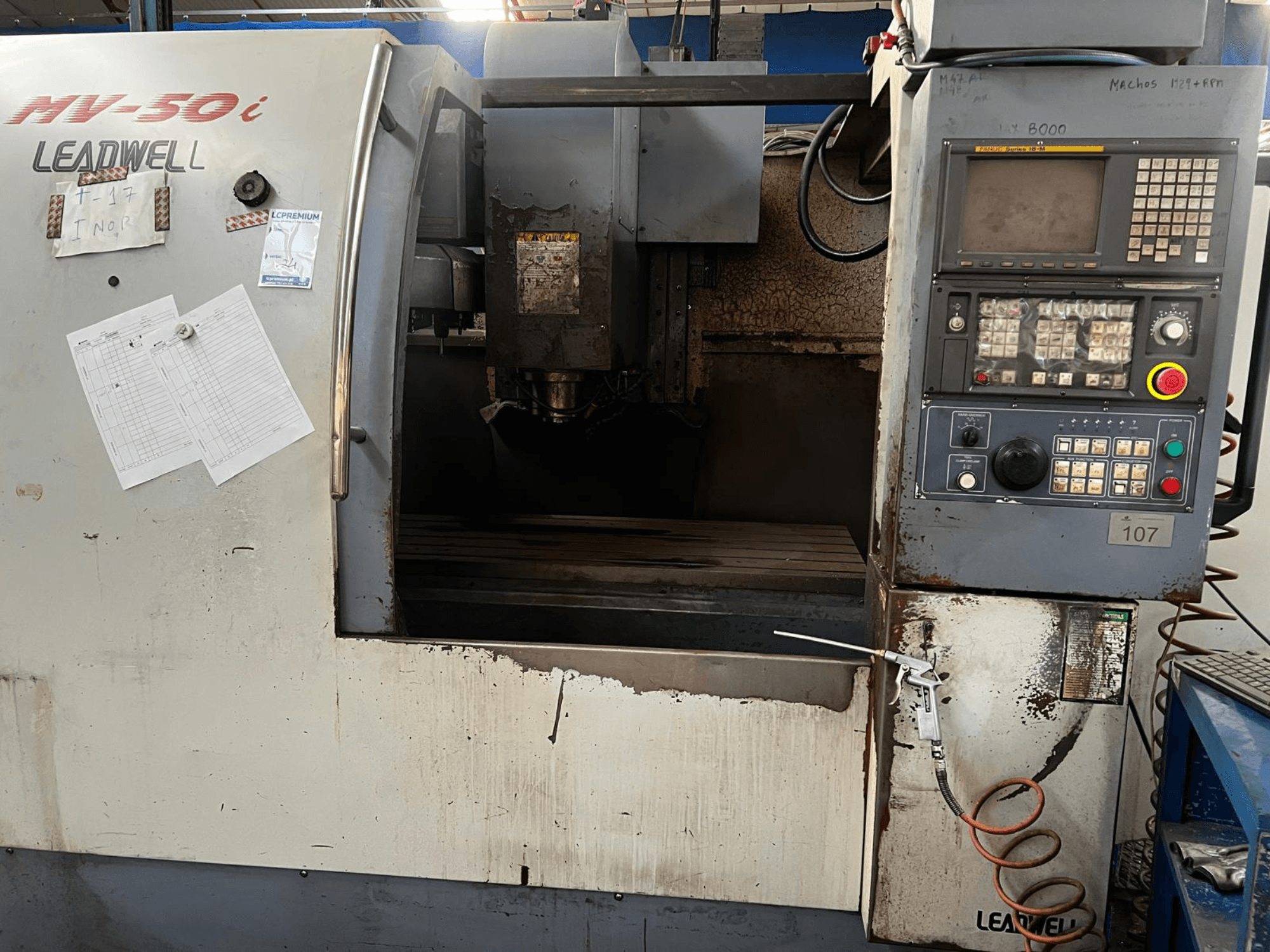 Vertikalusis apdirbimo centras „Leadwell MV-50i“, vaizdas iš priekio, kuriame matomas valdymo pultas, suklio zona ir darbo stalas su nusidėvėjimo žymėmis.