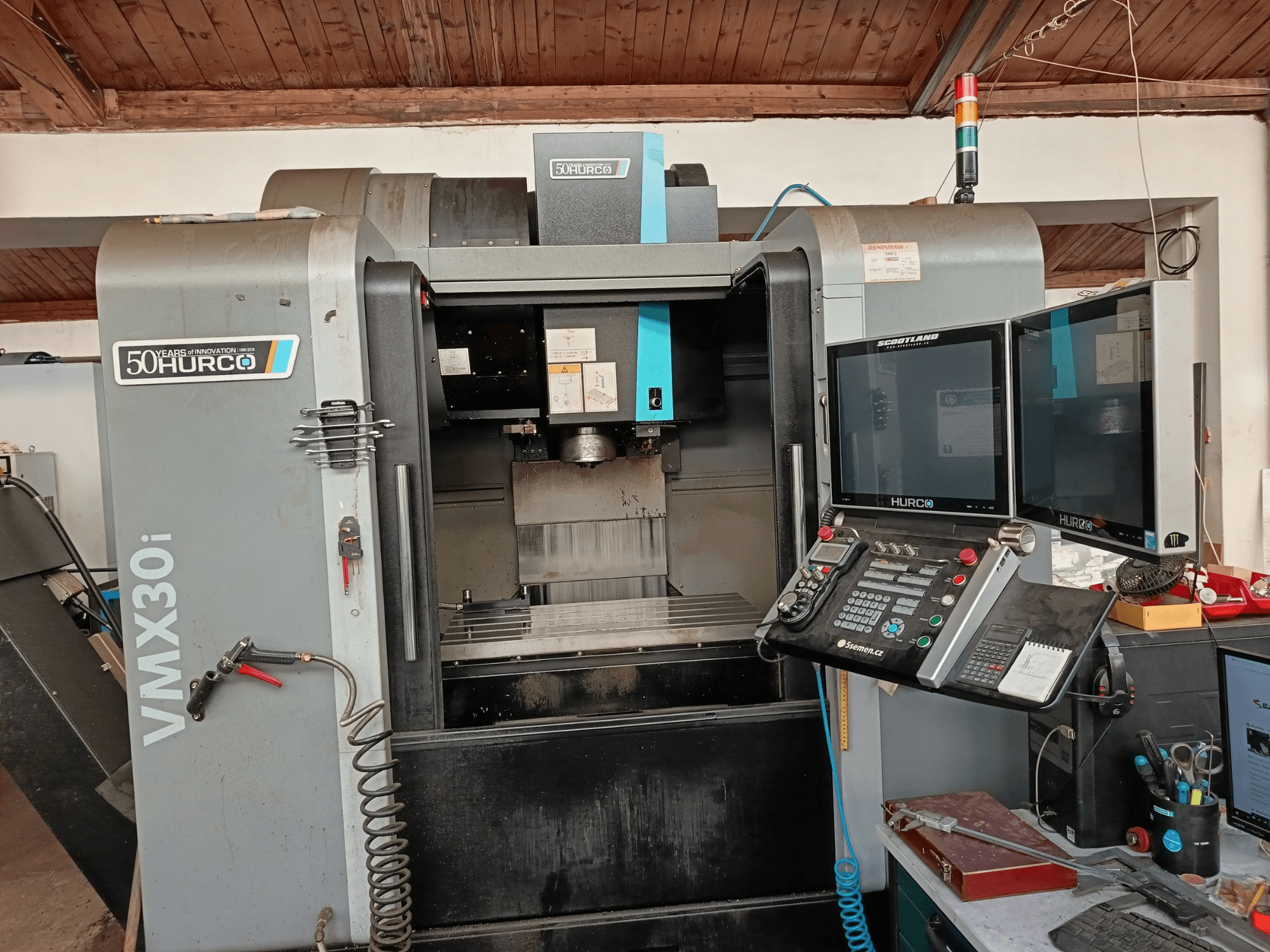 Hurco VMX30i CNC frezavimo staklės iš priekio, su dviem monitoriais, valdymo skydeliu ir prijungta žarna.