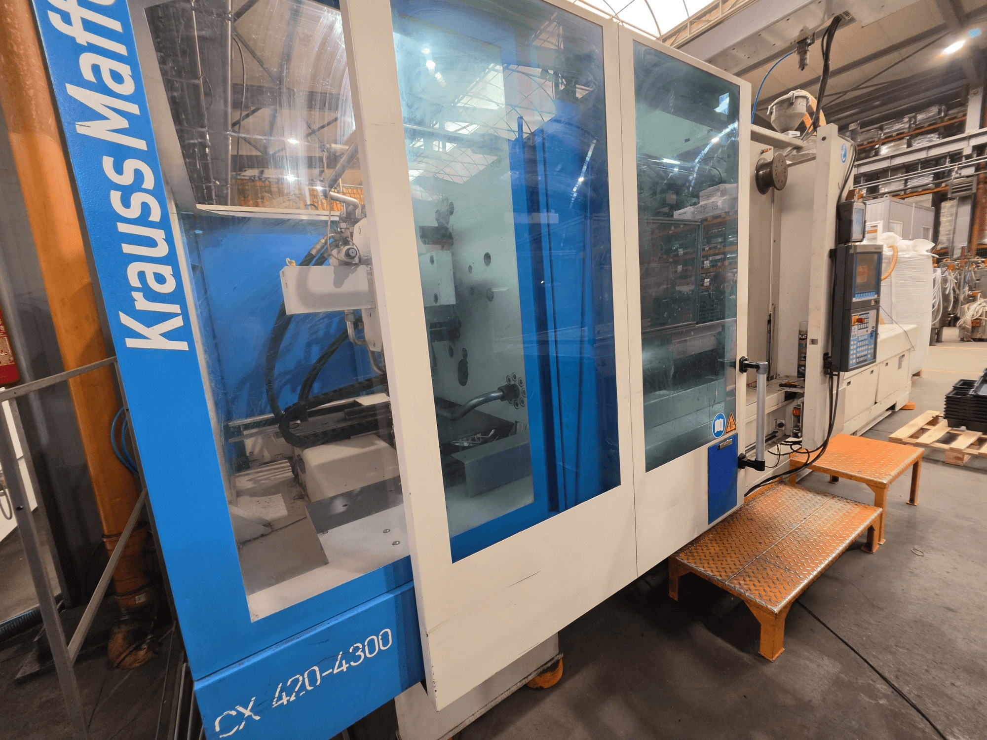 Krauss Maffei CX 420-4300 hidraulinė liejimo mašina, šoninis vaizdas, kuriame matyti valdymo pultas ir permatomos plokštės.