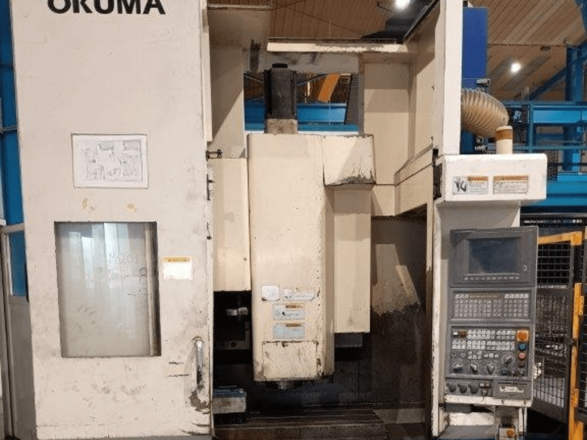 "Okuma" CNC frezavimo staklės, vaizdas iš priekio, valdymo skydelis su mygtukais, ekranas ir matomi ženklai ant staklių korpuso.
