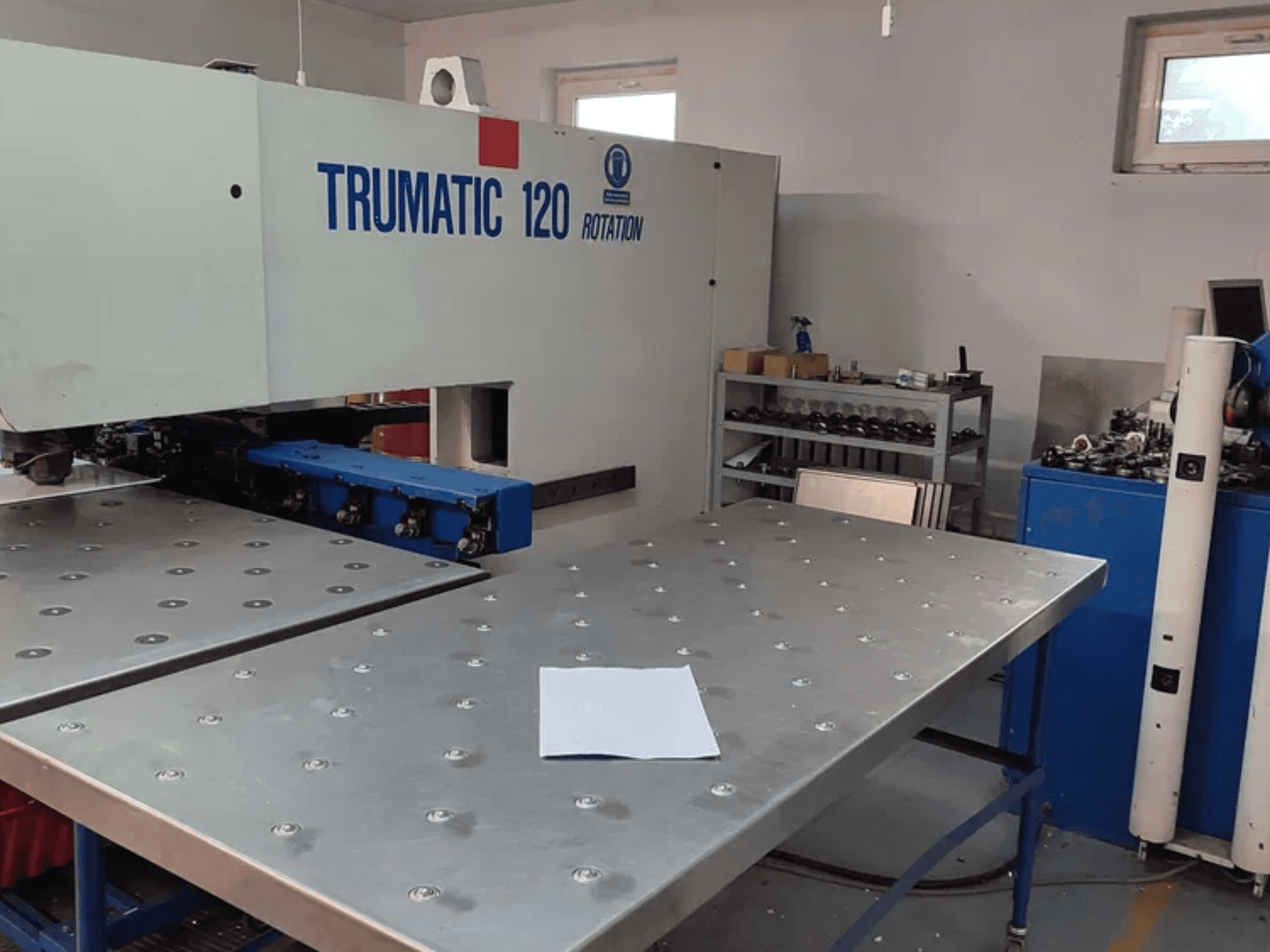 TRUMPF TRUMATIC 120R CNC perforavimo staklės, žiūrint iš priekio, su metaliniu stalu su perforuotomis skylėmis ir tuščiu lapu.