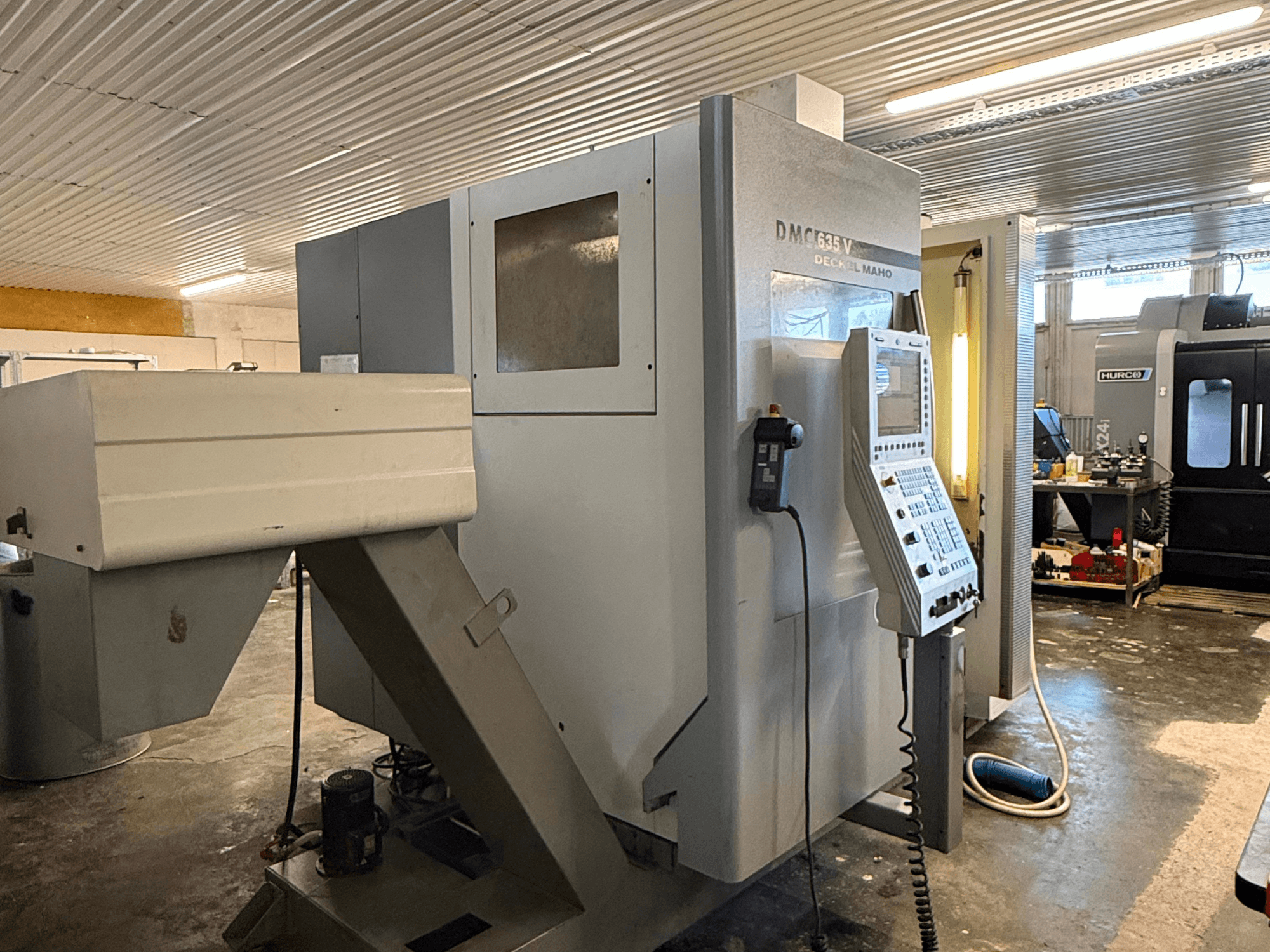 DMC G635V frezavimo staklės dirbtuvėse, vaizdas iš priekio, matomas valdymo skydelis ir prijungti elektriniai įrankiai.