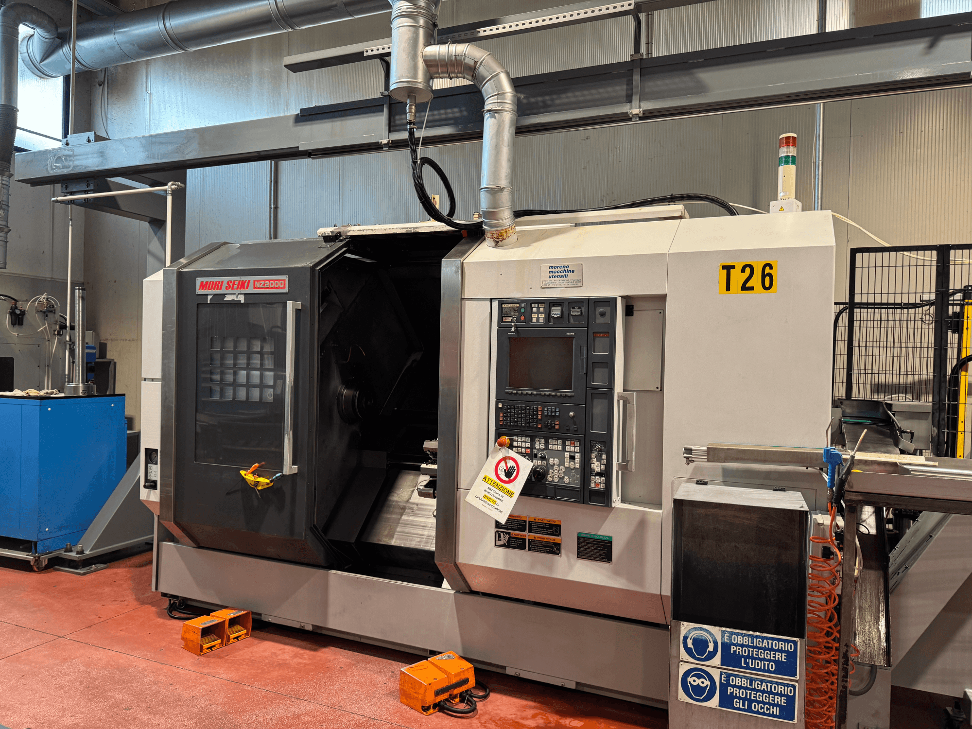 MORI SEIKI NZ-2000/T2/Y2 tekinimo frezavimo centras, vaizdas iš priekio, su valdymo skydeliu, saugos ženklais ir pramonine sąranka.