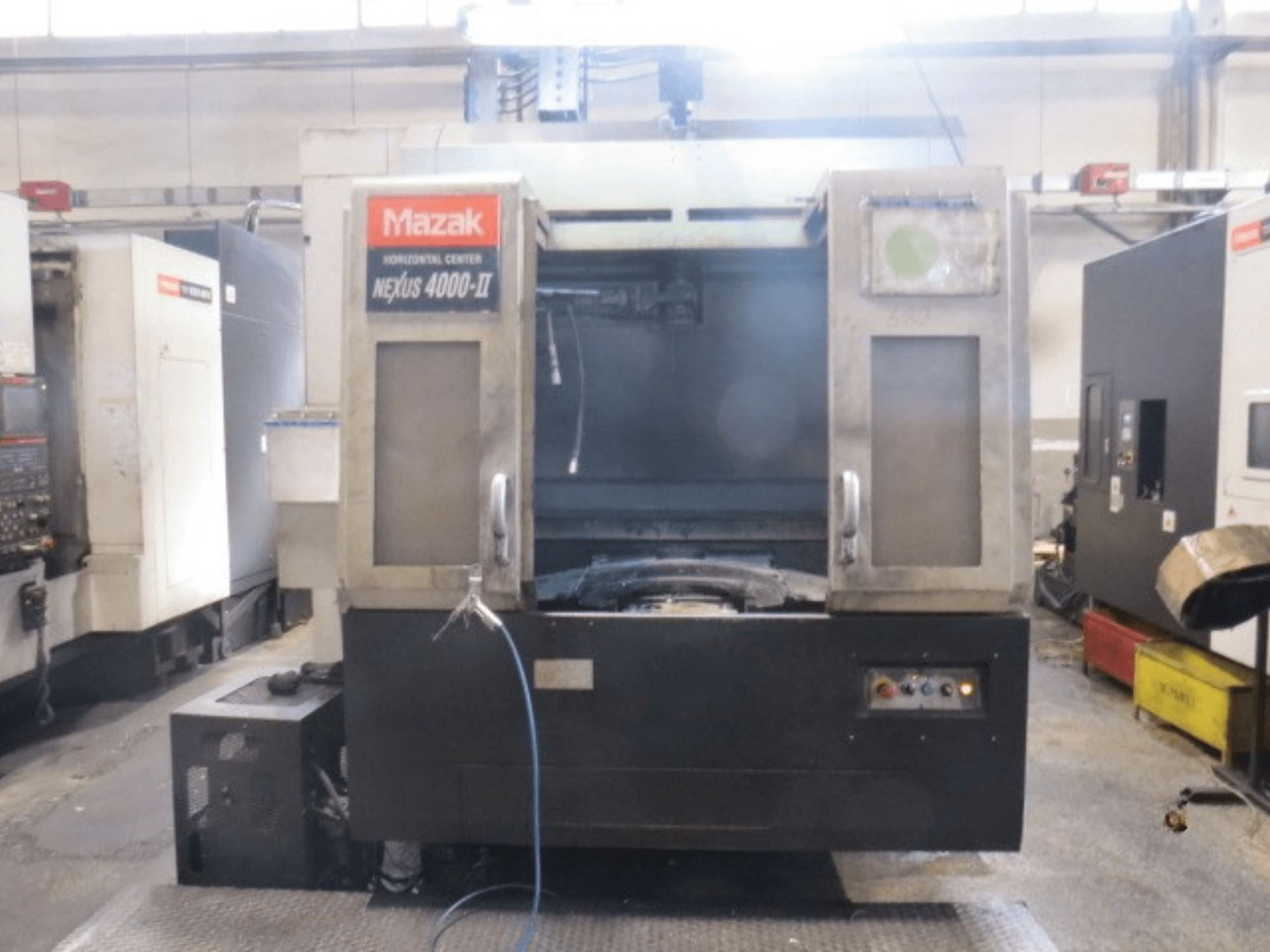 „Mazak NEXUS 4000 II“ horizontalus apdirbimo centras, vaizdas iš priekio, kuriame matomas valdymo pultas, aušinimo skysčio tiekimo sistema ir atvira darbo zona.