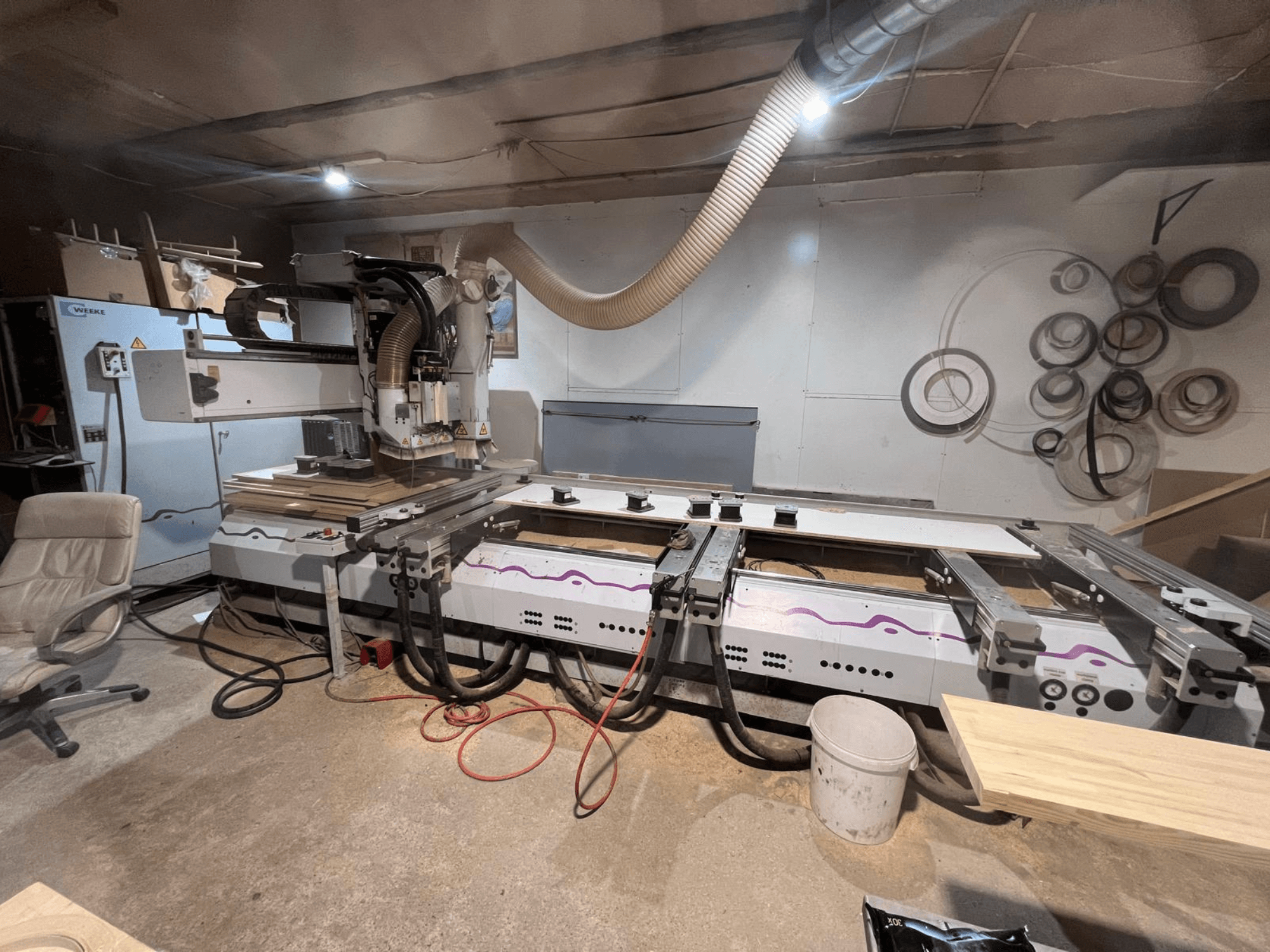CNC medžio apdirbimo centras „Weeke OPTIMAT BP 120“ dirbtuvėse, vaizdas iš priekio, ant paviršiaus matomi medžio gabalai ir įrankiai.