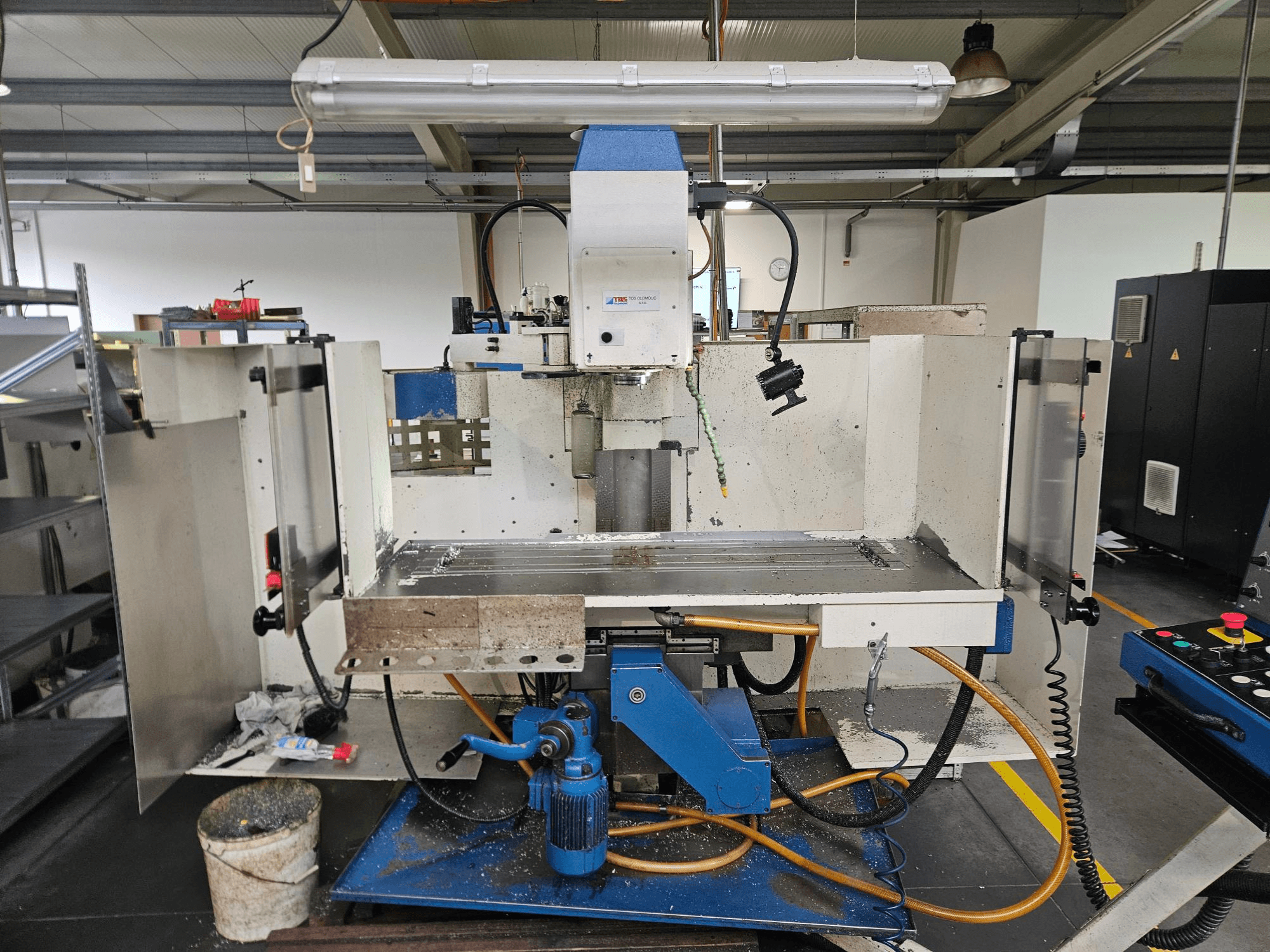TOS Olomouc FV30 CNC Vertikalus apdirbimo centras dirbtuvėse, priekinis vaizdas, kuriame matomas valdymo skydelis, stalas ir aušinimo skysčio sistema.