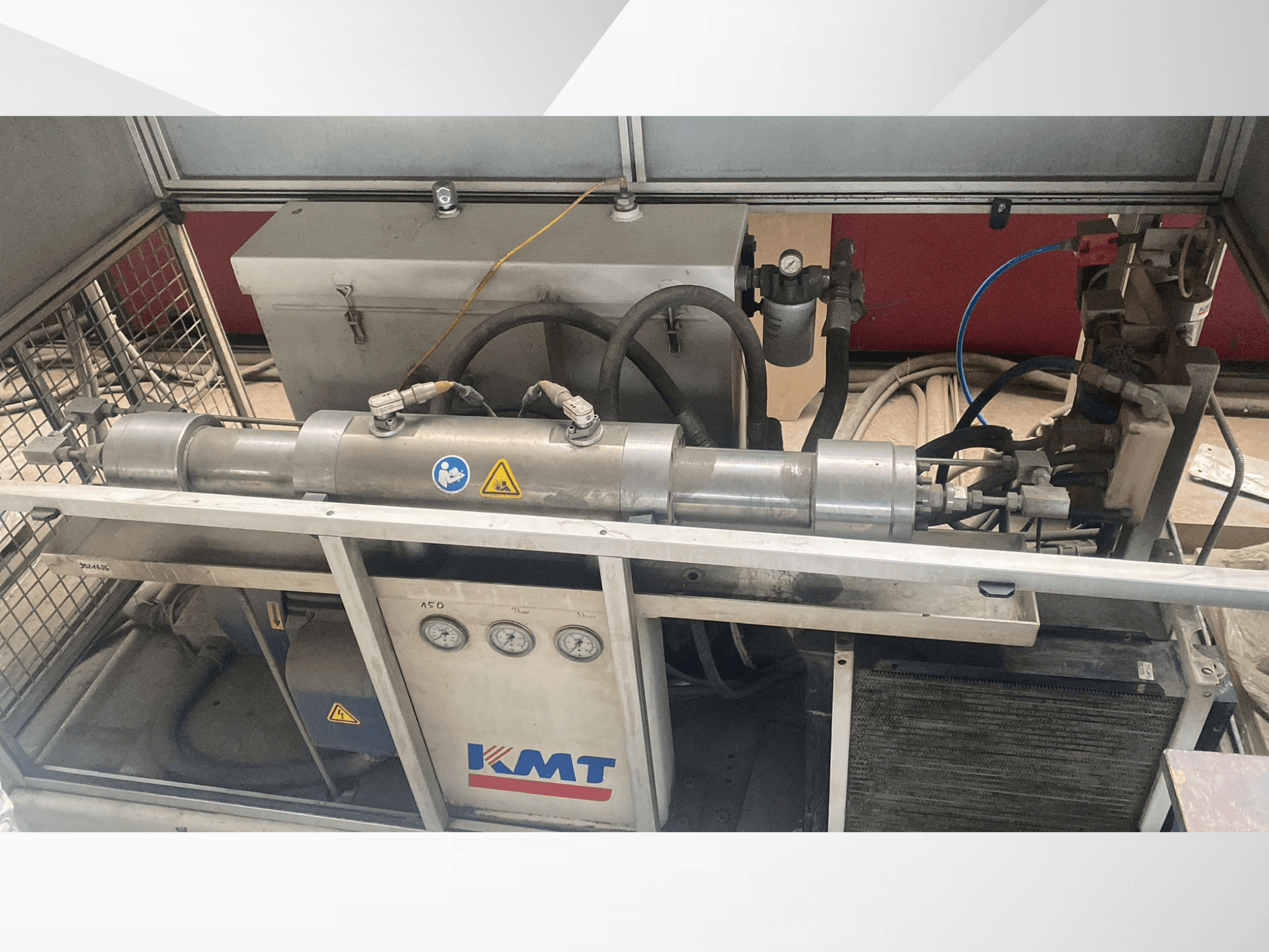 KMT hidraulinė mašina iš priekio, su manometrais, žarnomis ir metaliniu korpusu, idealiai tinkanti naudoti pramonėje.