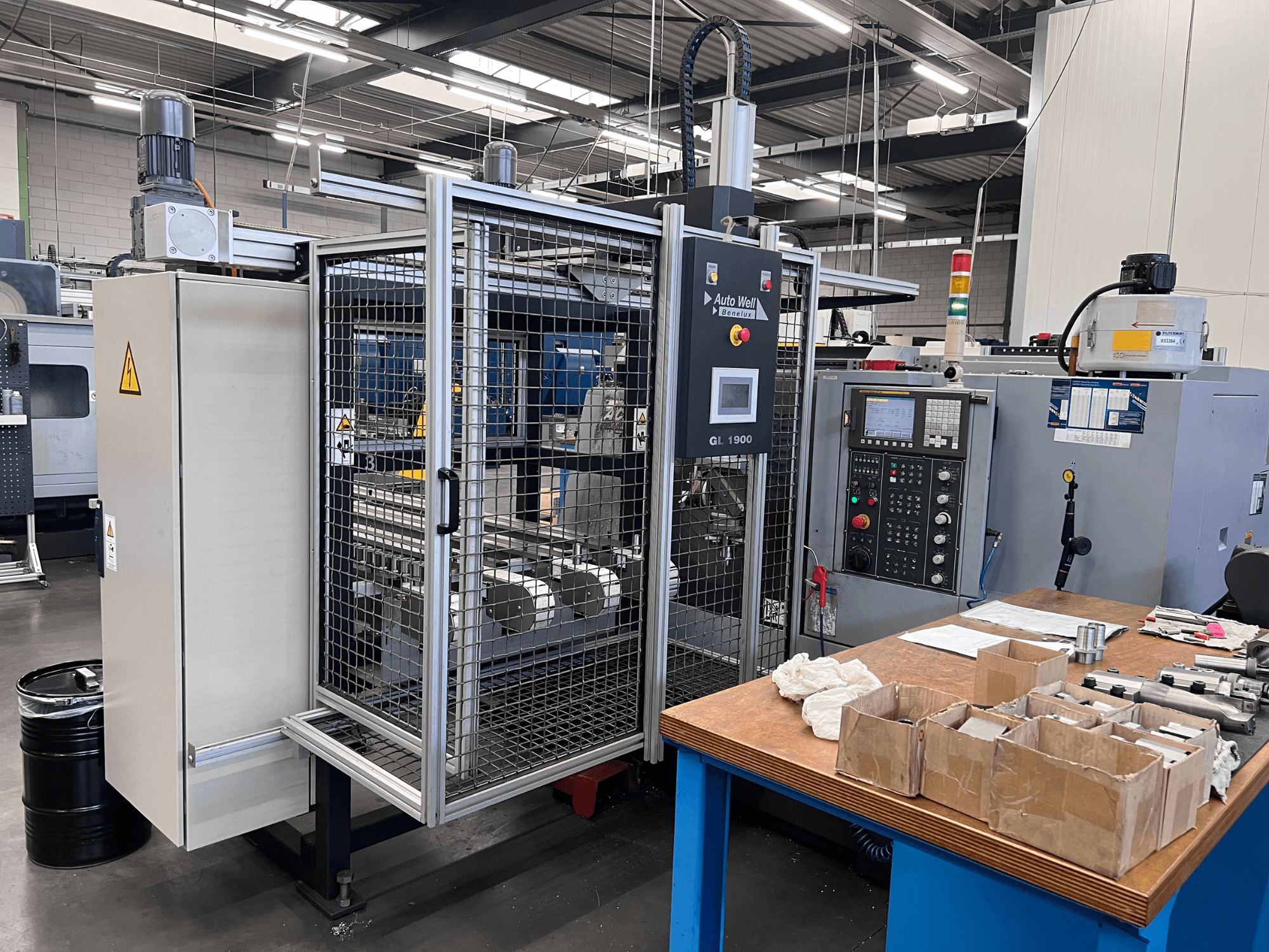 Įrenginio "Auto Weld GL 1900" su valdymo skydeliu, apsauginiu gaubtu ir aplinkiniais įrankiais ant darbo stalo vaizdas iš priekio.