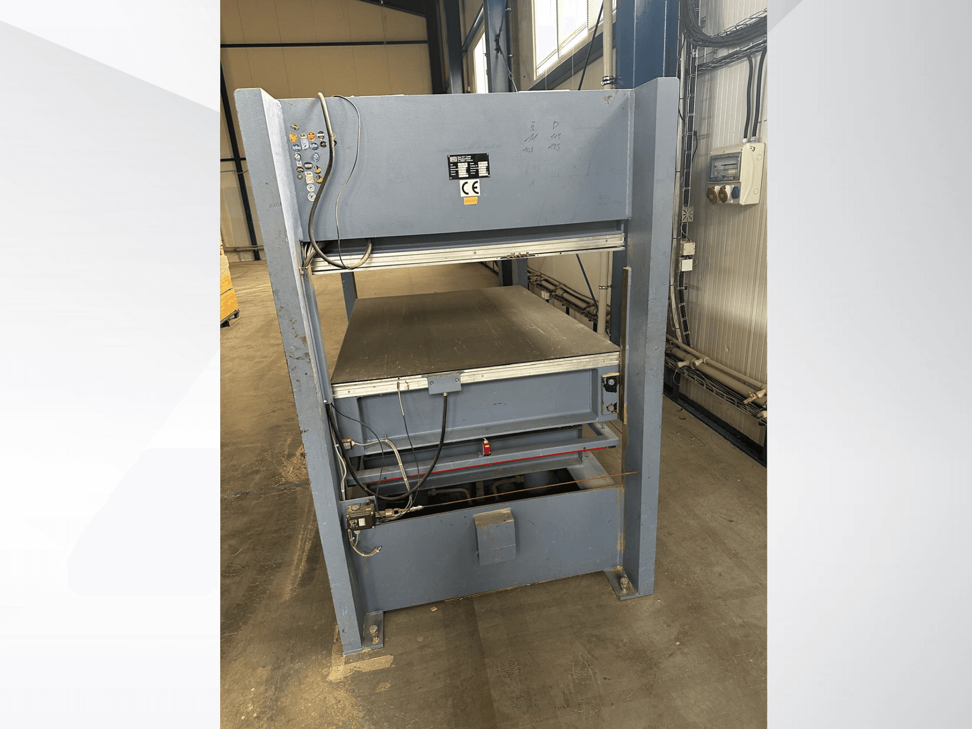 Pilka pramoninė mašina su valdymo skydeliu, žiūrint iš priekio; su reguliuojamomis platformomis ir saugos ženklais.