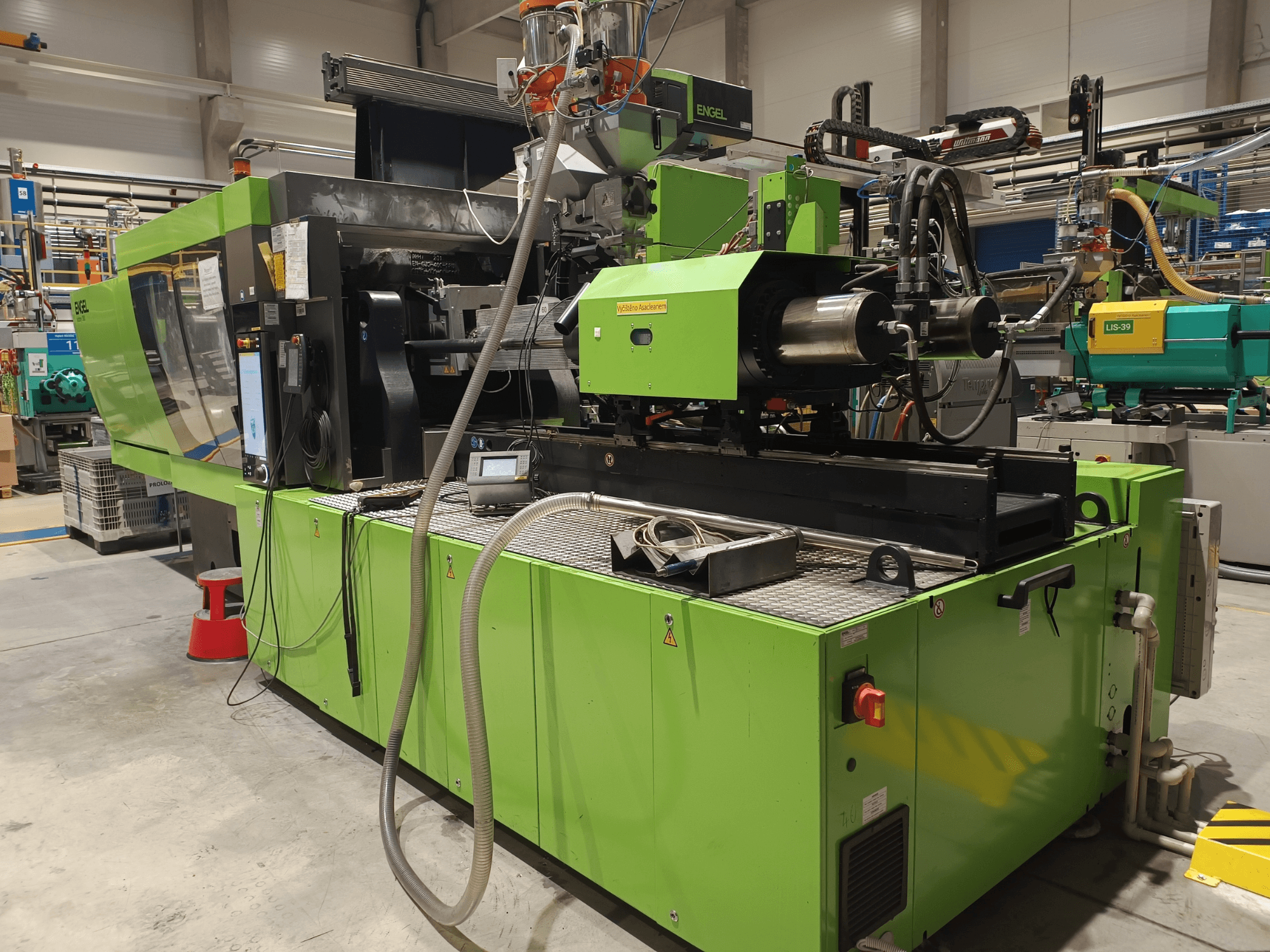 Šoninis vaizdas, žalios spalvos išorė, matomas jutiklinio ekrano skydelis ir hidrauliniai komponentai.