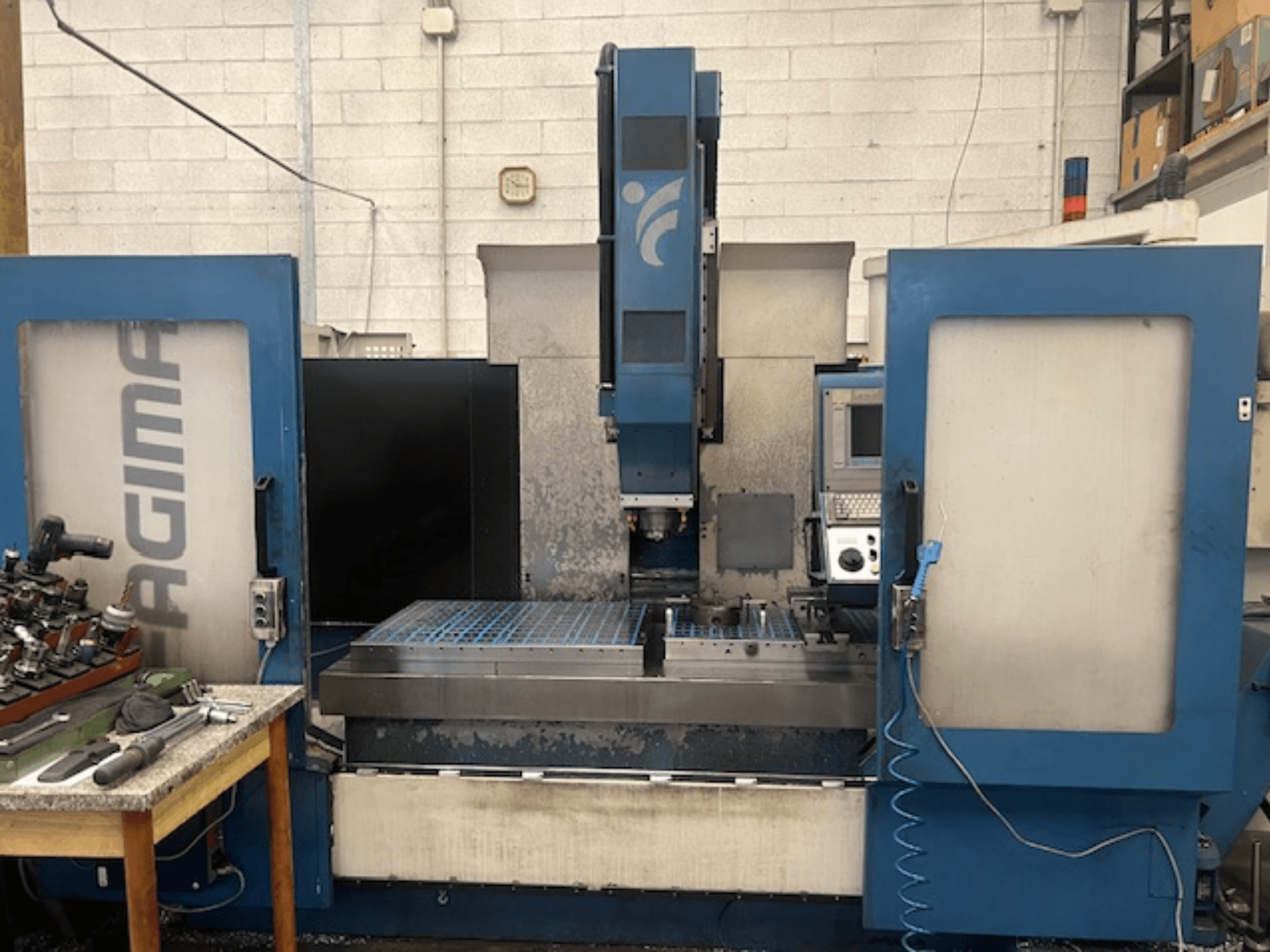 JAGIMA CNC staklių vaizdas iš priekio su didele metaline darbo vieta, matomu valdymo pultu ir įrankiais ant šalia esančio stalo.