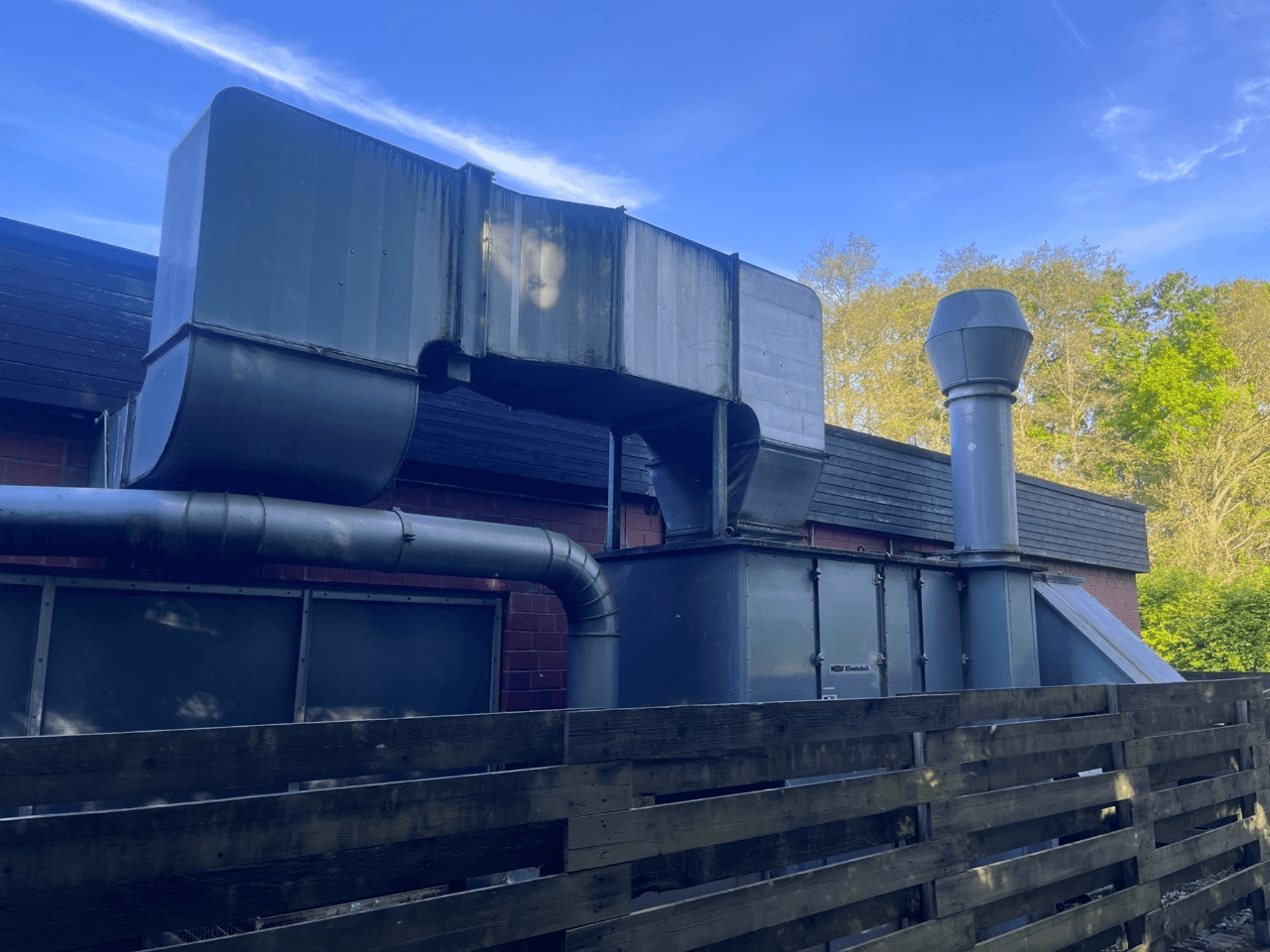 Pramoninė vėdinimo sistema su metaliniais ortakiais, vaizdas iš šono; įskaitant kvadratinį ir cilindrinį kaminą, žalia apdaila.