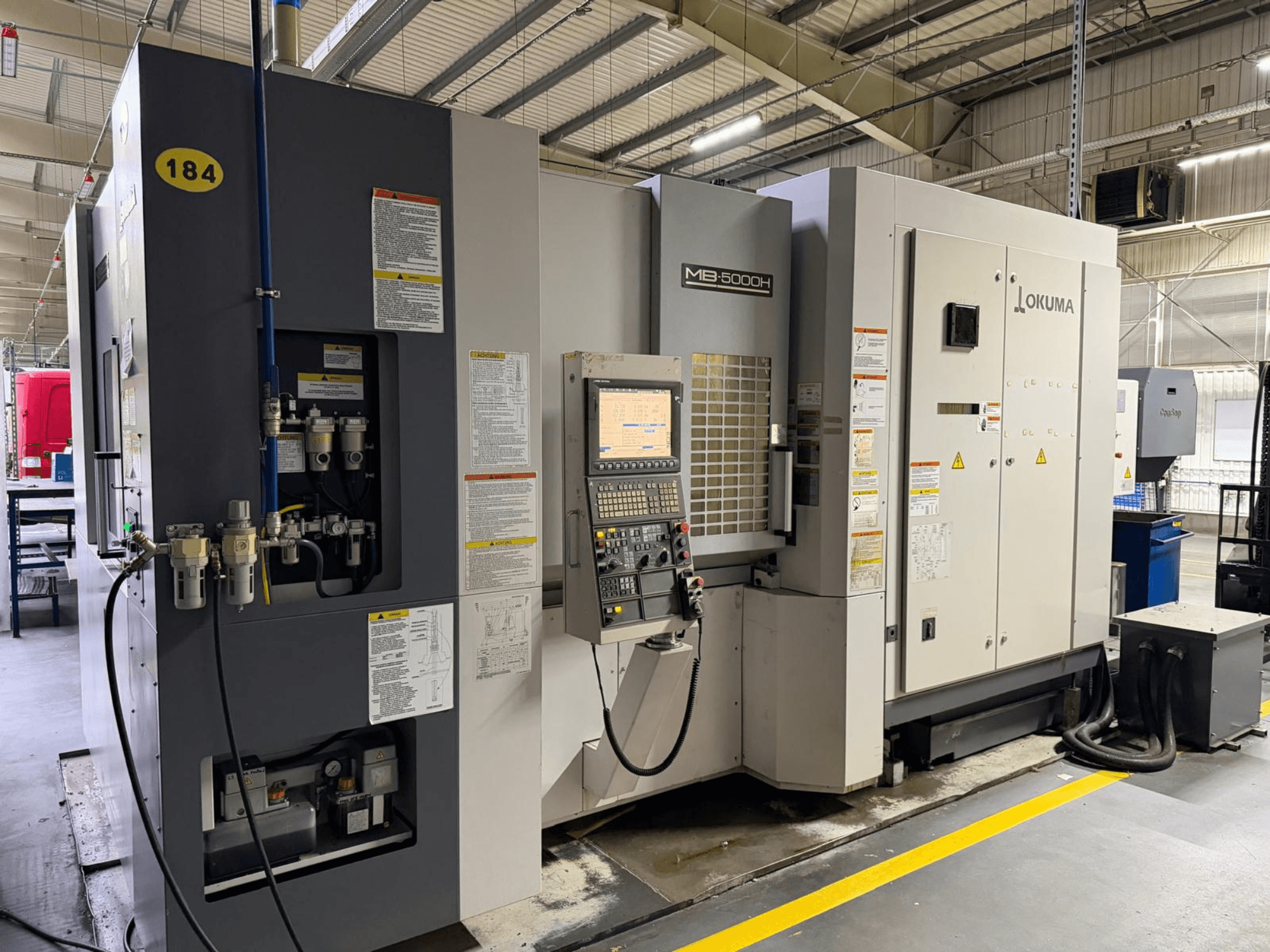 Okuma MB 5000H horizontalaus apdirbimo centro priekinis vaizdas, kuriame matomi valdikliai, ženklinimas ir hidraulinės jungtys.