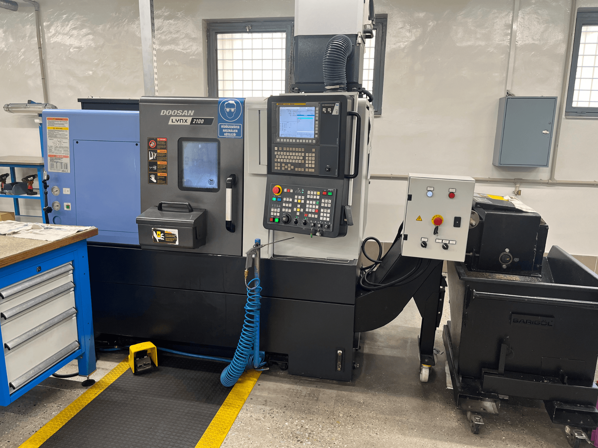 Doosan Lynx 210 tekinimo staklės dirbtuvėse, kuriose matomas valdymo skydelis, įrankių laikymo vieta ir aušinimo skysčio sistema, šoninis vaizdas su darbo vietos detalėmis.