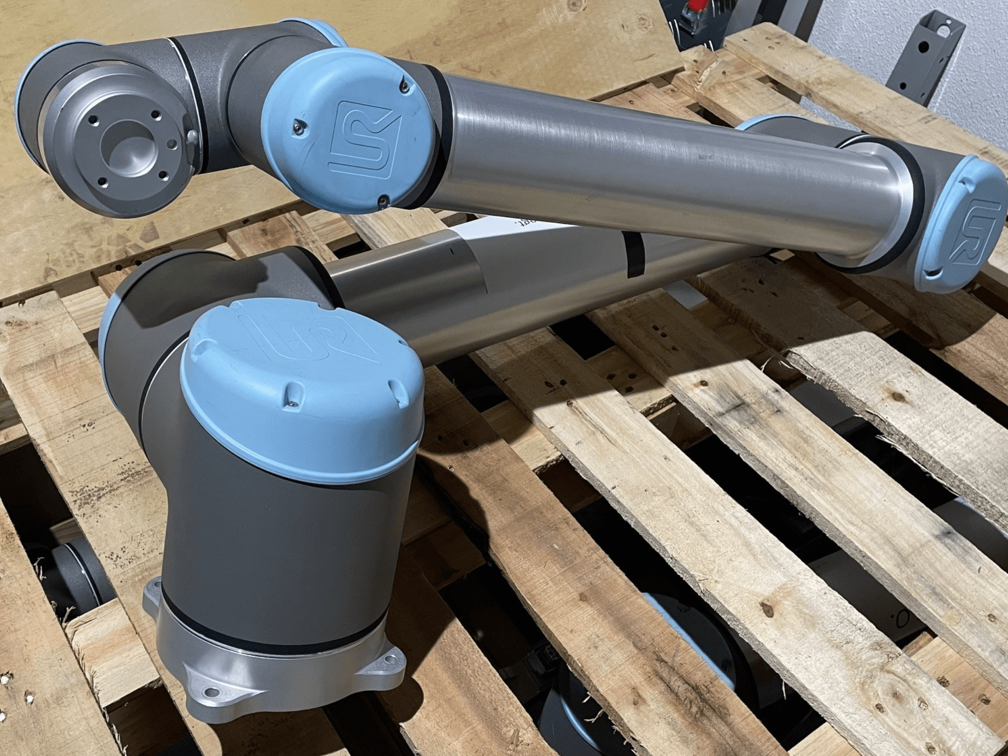 Sidabrinė roboto ranka su mėlynais galiniais dangteliais, vaizdas iš priekio, matomi sąnariai ir mechaninės detalės, padėta ant medinio padėklo.