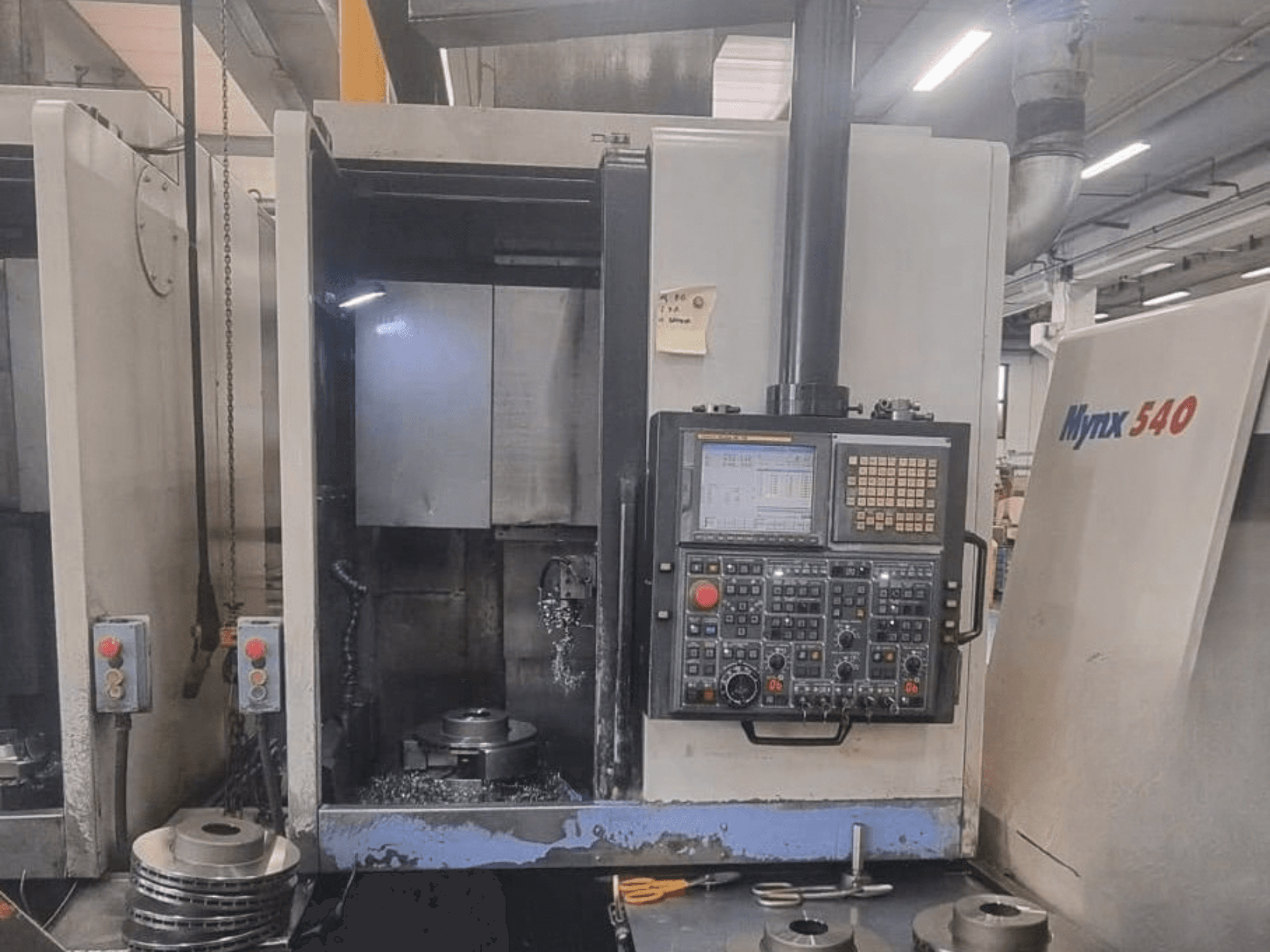 „DOOSAN PUMA V400-2SP“ vertikalios tekinimo staklių vaizdas iš priekio, kuriame matomas valdymo pultas ir staklių viduje įrengtas ruošinys.