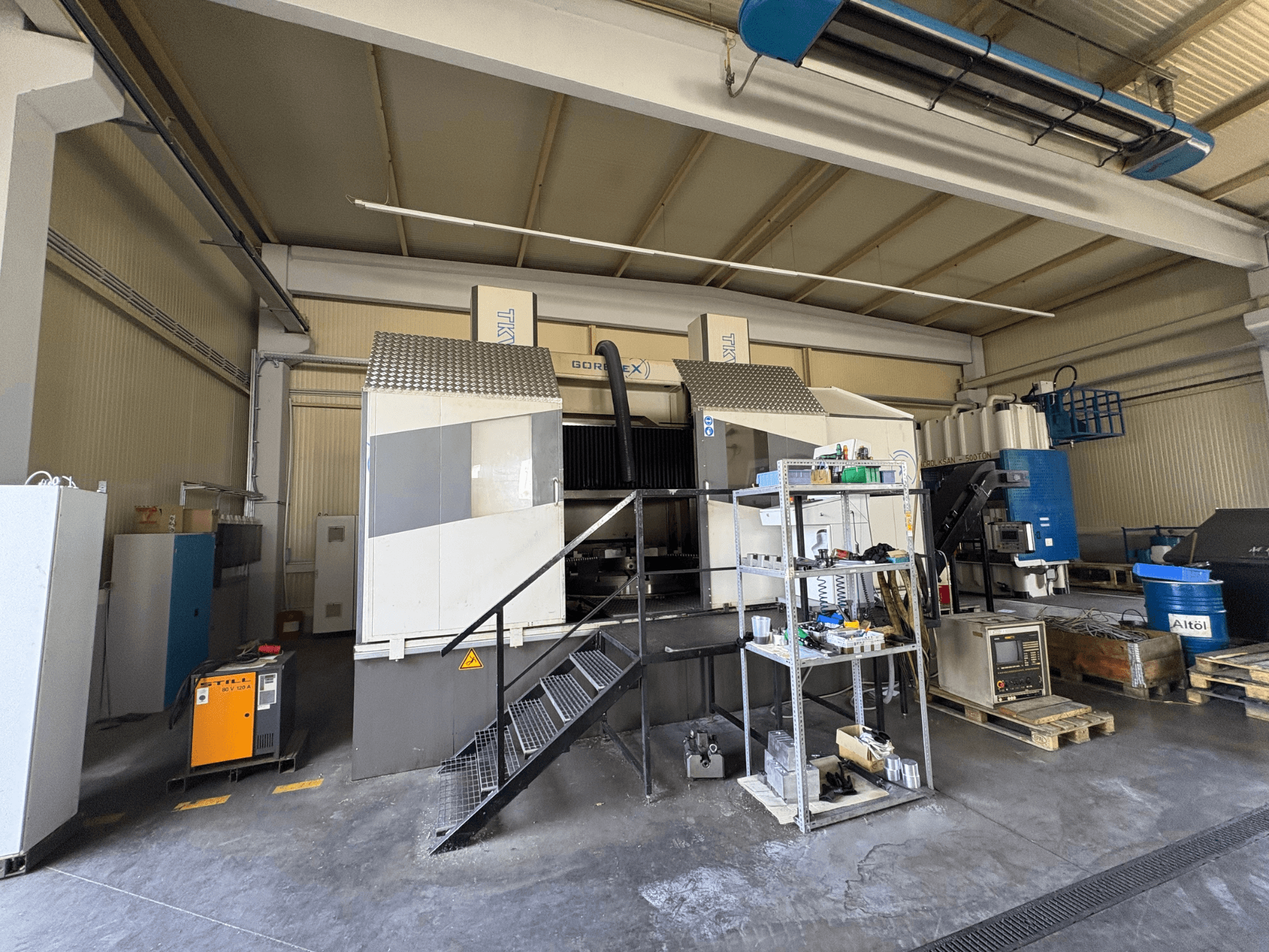 Pramoninio apdirbimo įrenginys su GORAT X staklėmis, vaizdas iš šono; apima įrankius, valdymo pultą ir įrangą ant lentynų.