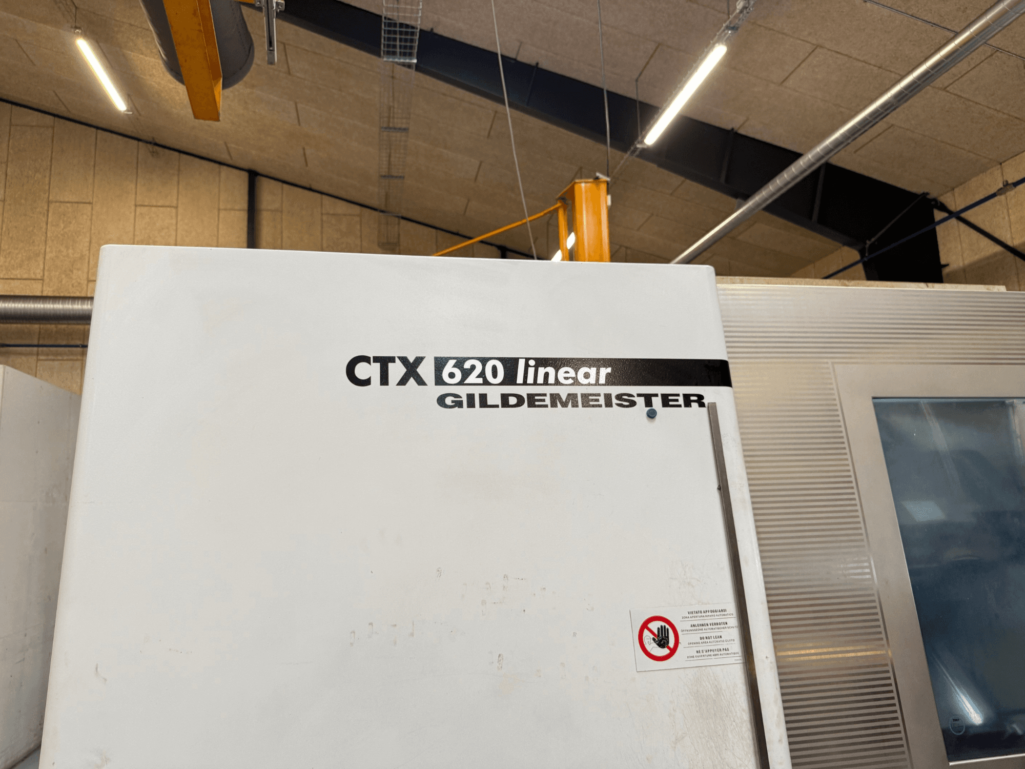 CTX 620 Linear Gildemeister mašinos vaizdas iš šono, balta išorė ir įspėjamosios saugos etiketės.