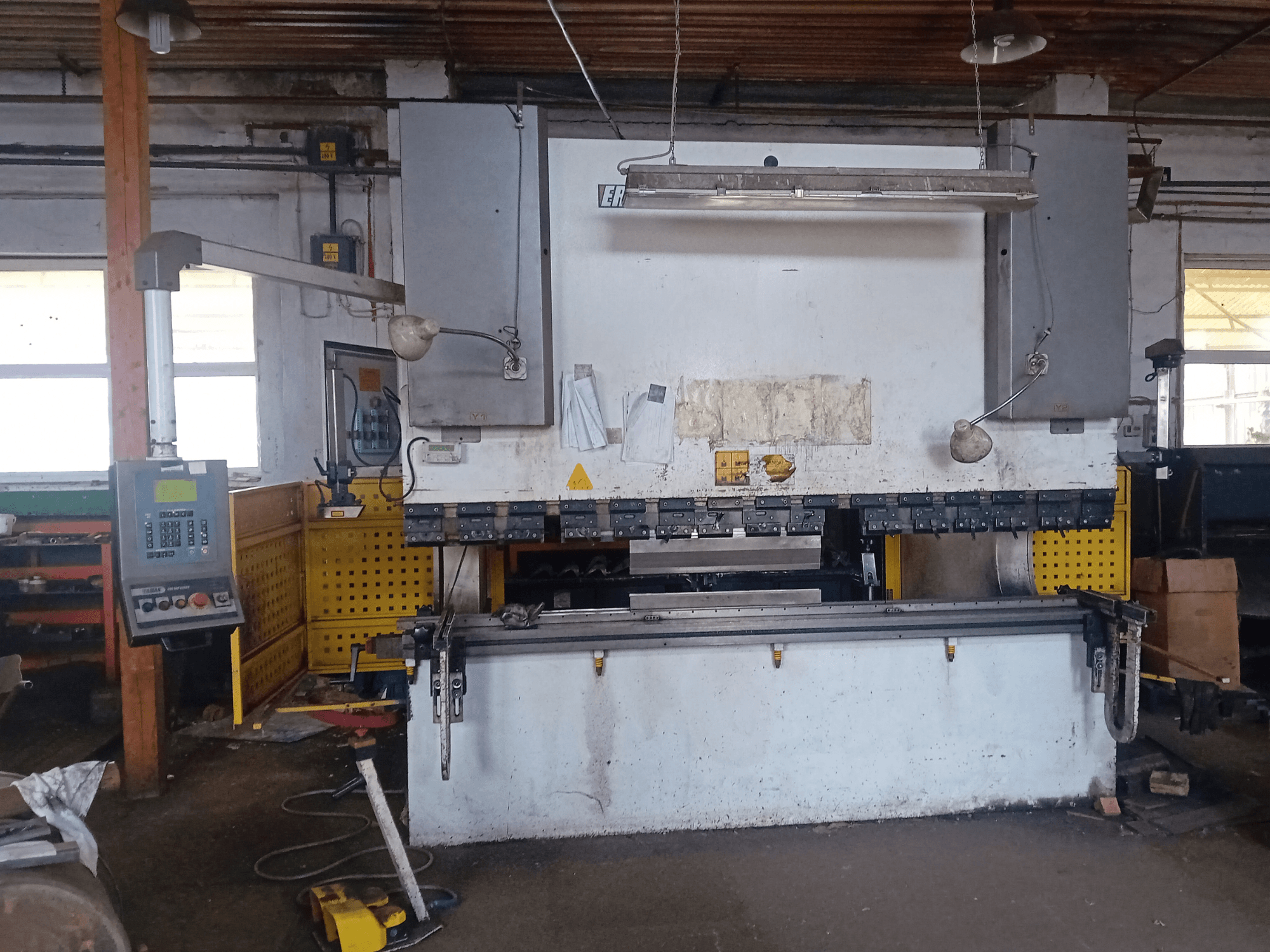 ERMAK CNC HAP 3100x300 hidraulinis presas, parodytas iš priekio, su valdymo pultu ir darbo stalu dirbtuvėse.