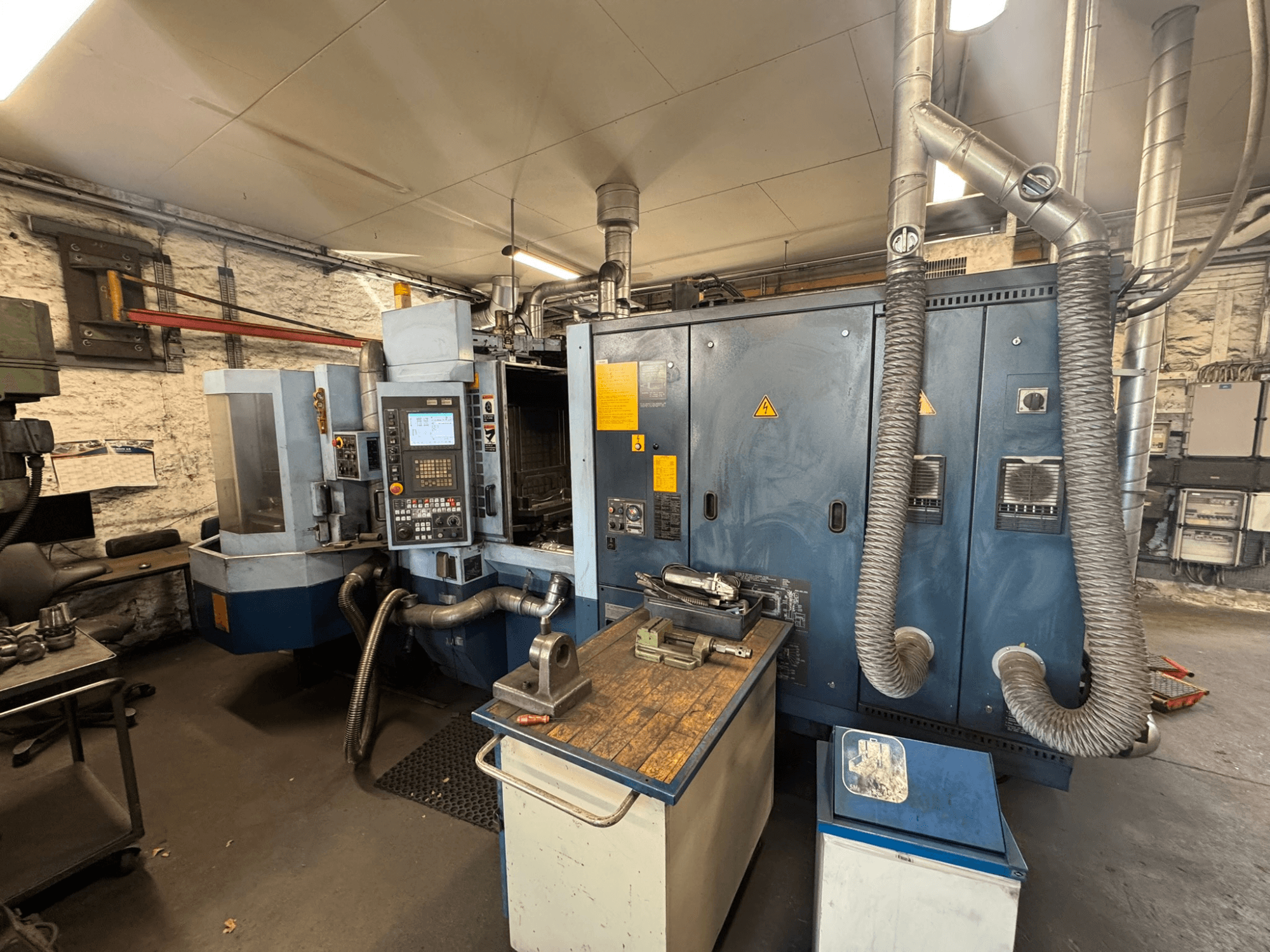 Matsuura H.PLUS-300 horizontalus apdirbimo centras dirbtuvėse, vaizdas iš priekio, kuriame matomas valdymo pultas ir darbo stalas.