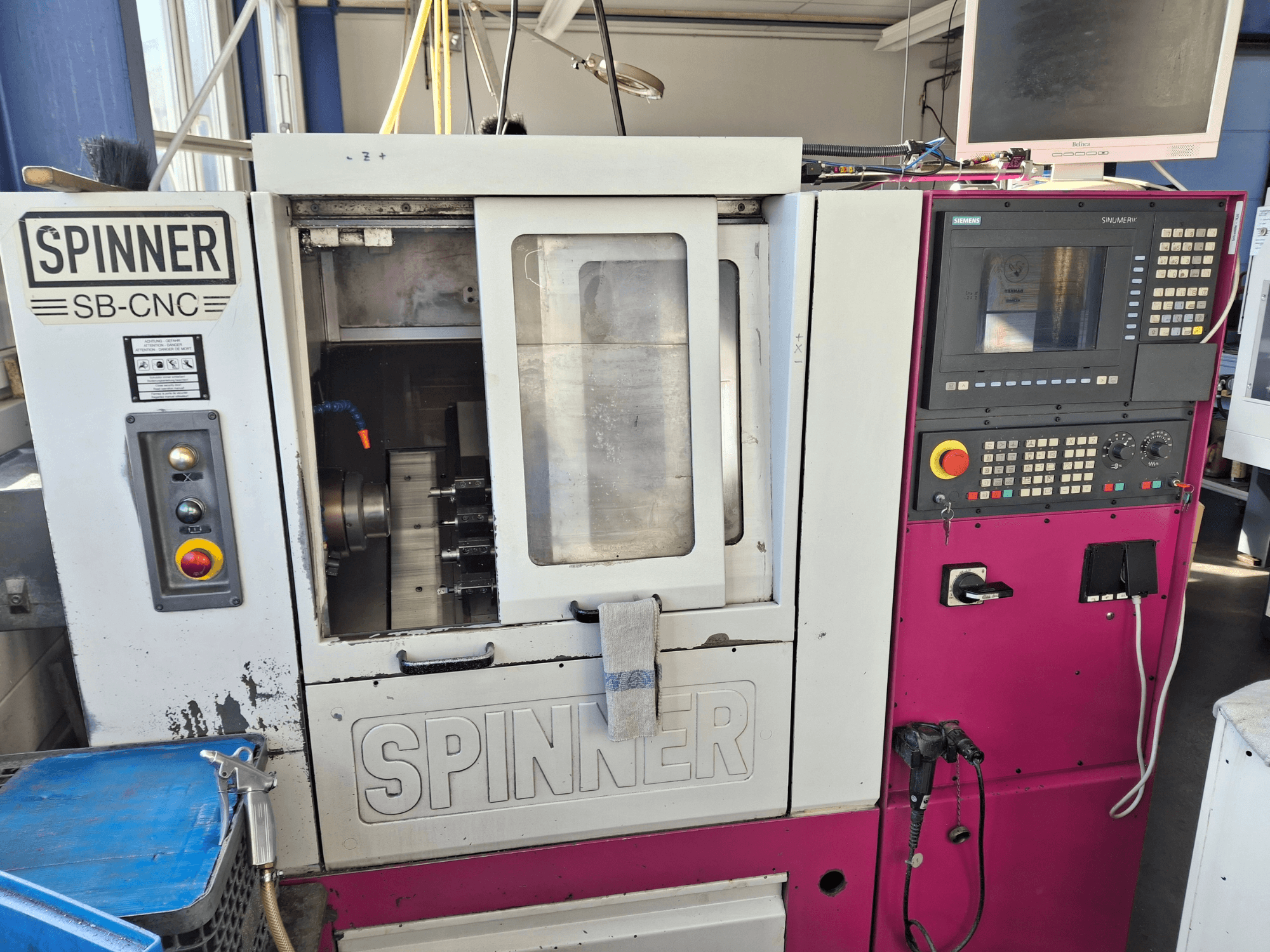 Horizontalios tekinimo staklės SPINNER SB-CNC, priekinis vaizdas, kuriame matyti valdymo skydelis, įrankių laikiklis ir veikimo indikatoriai.