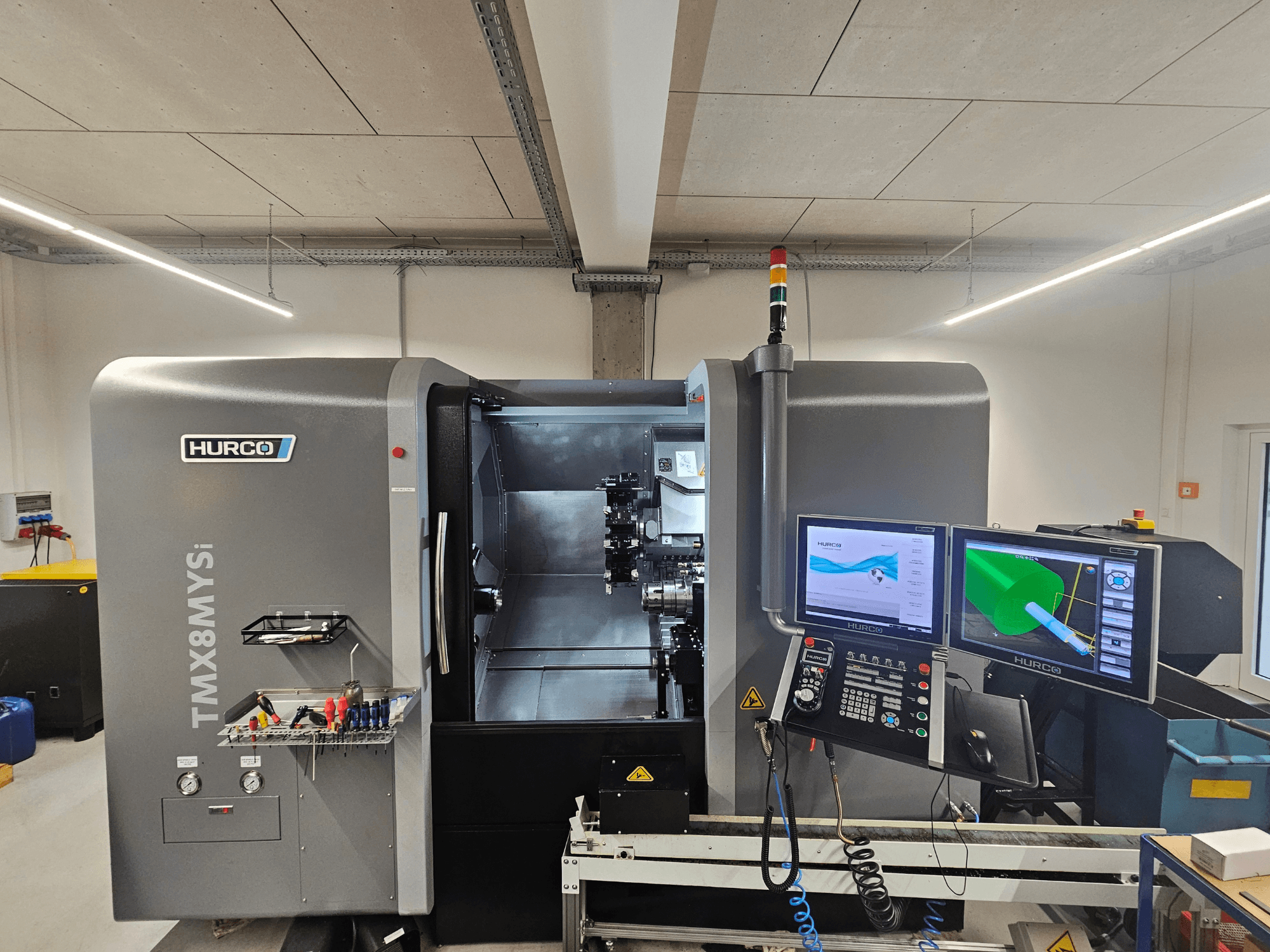 "Hurco TMX 8 MYSi" tekinimo frezavimo centras dirbtuvėse su dviem monitoriais, valdymo skydeliu ir įrankiais šone.