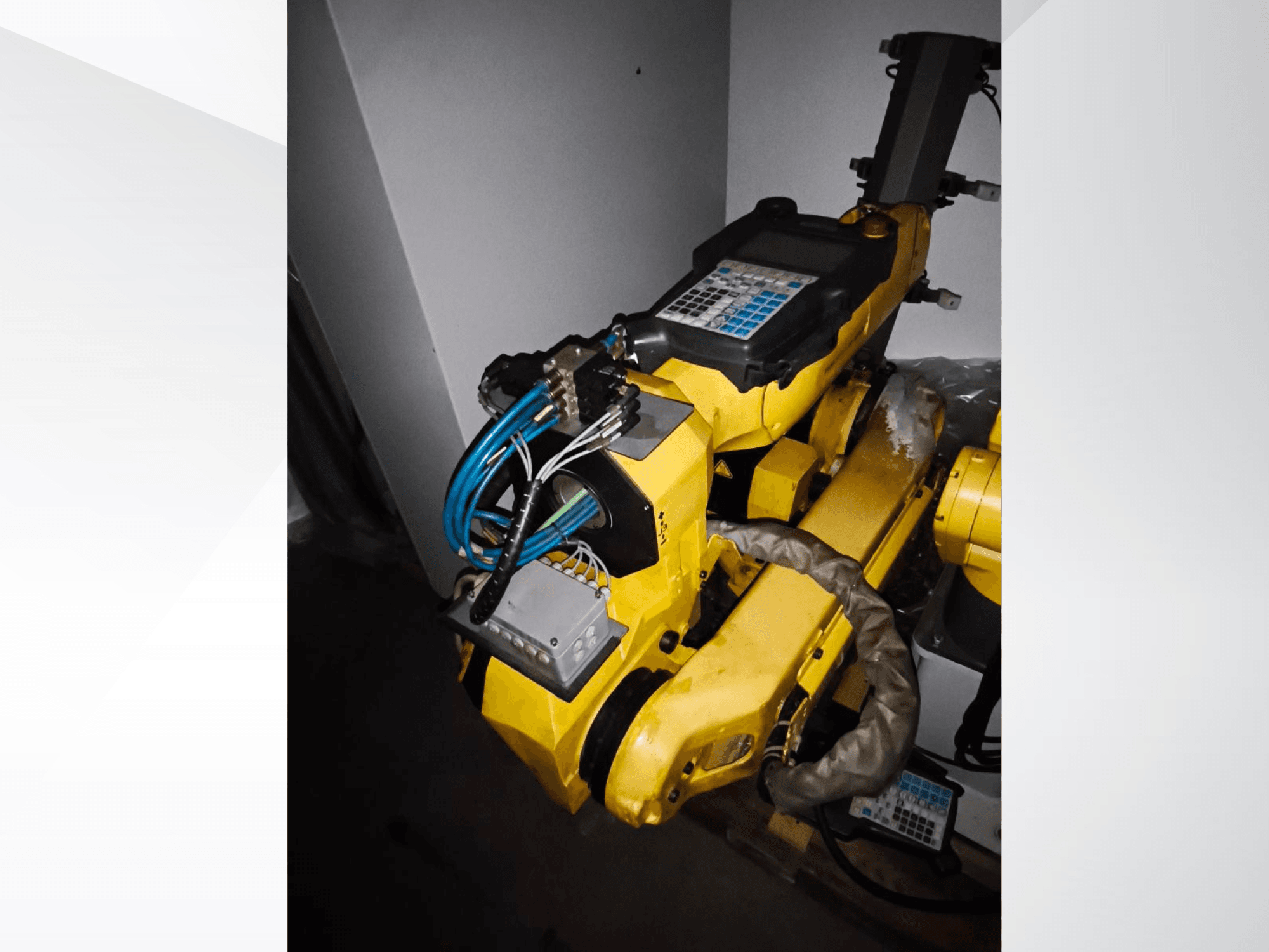 FANUC M-20iA roboto rankos šoninis vaizdas, kuriame matyti geltonas korpusas, valdymo skydelis ir prijungti laidai.