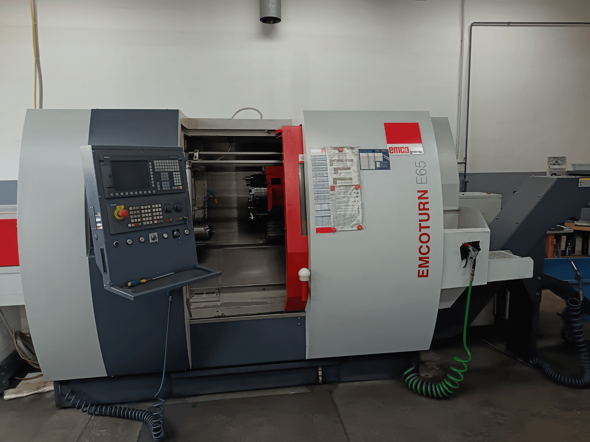 EMCO EMCOTURN E65 tekinimo frezavimo centras, priekinis vaizdas, rodantis valdymo skydelį, vidinį mechanizmą ir funkcijas dirbtuvėse.