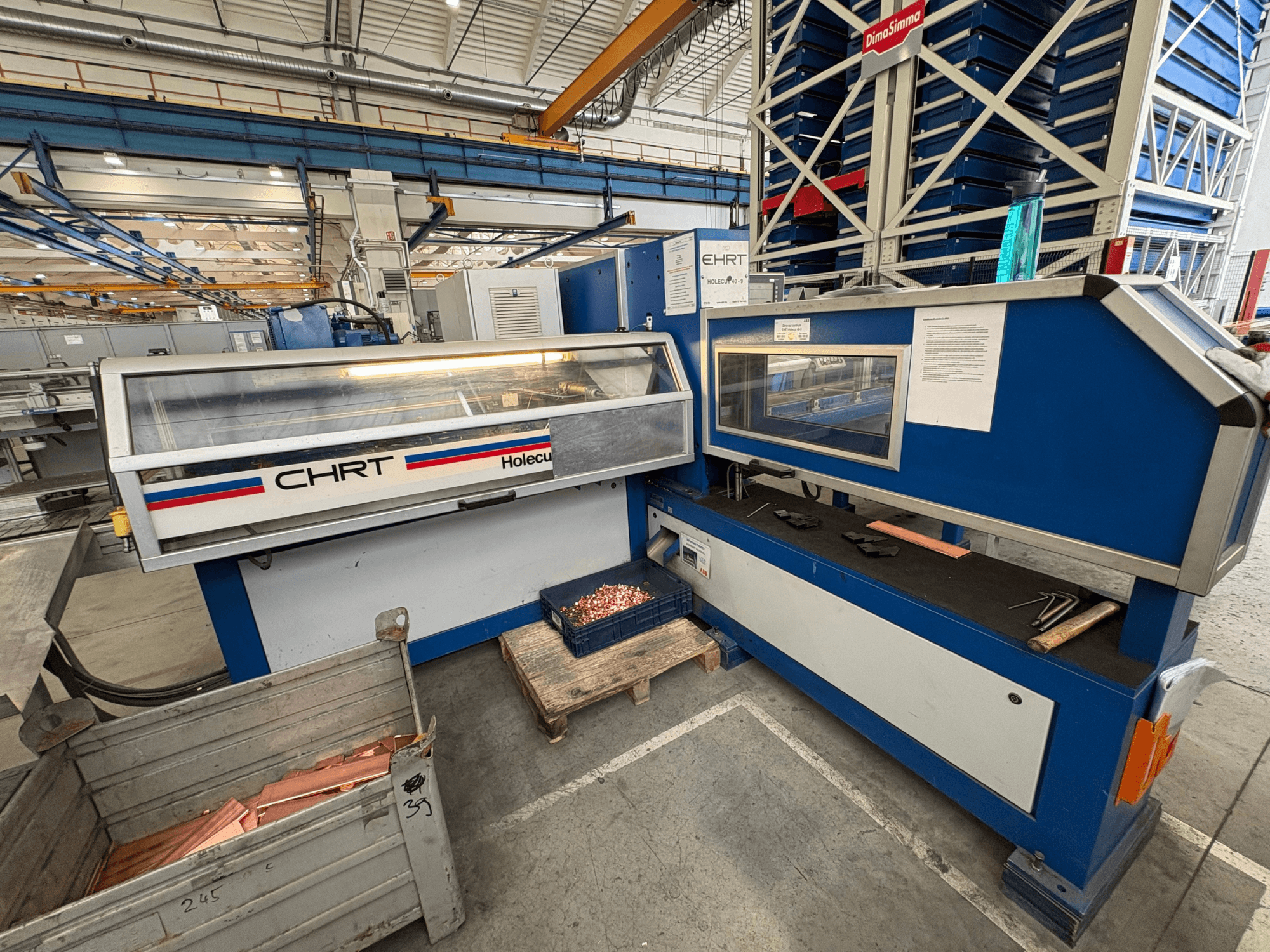 CNC perforavimo staklės EHRT Holecut 40-9, vaizdas iš priekio, su valdymo skydeliu, metaline dėže ir vario lakštais šalia.