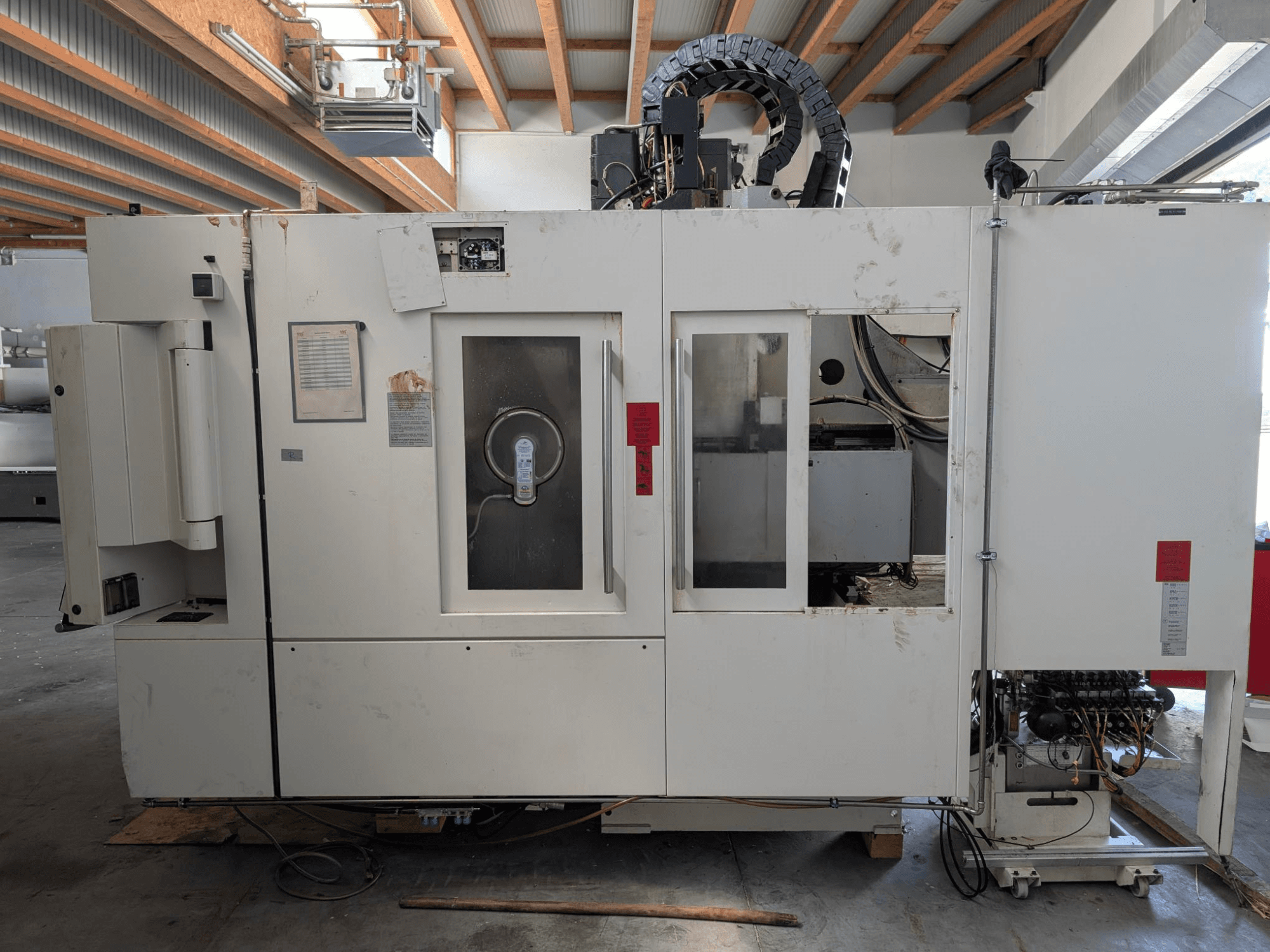 STAMA MC 326 vertikalusis apdirbimo centras, šoninis vaizdas, kuriame matomas valdymo skydelis, suklio sritis ir įvairios etiketės ant staklių.