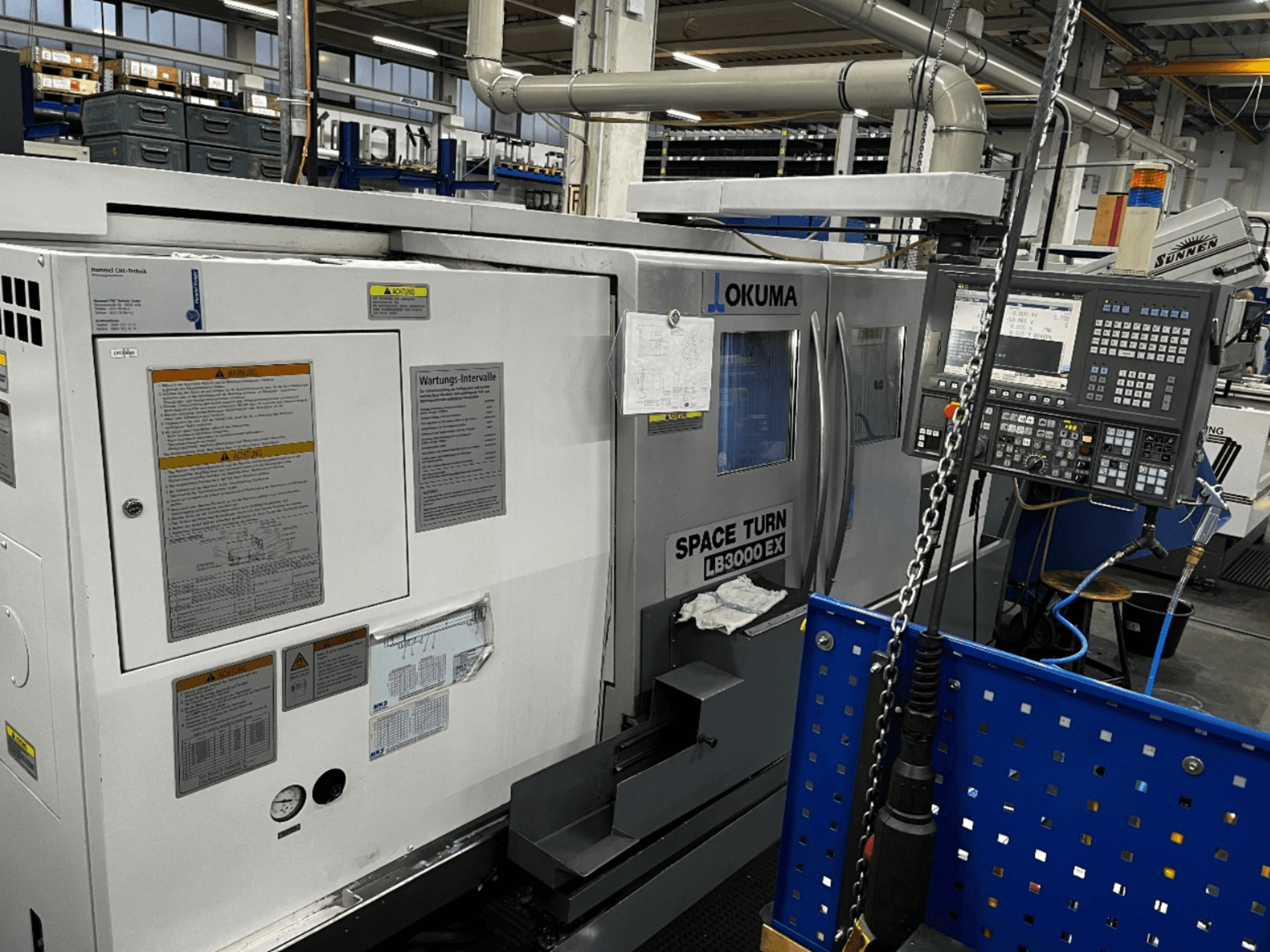 Okuma LB3000 EX horizontalios tekinimo staklės, vaizdas iš priekio, šone matomas valdymo skydelis ir saugos informacija.