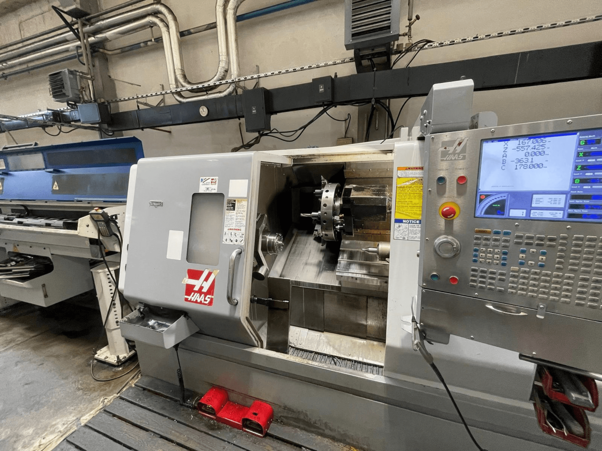 Dirbtuvėse esantis horizontalus tekinimo staklės „Haas SL-30THE“, turinčios skaitmeninį valdymo pultą ir atvirą darbo zoną.