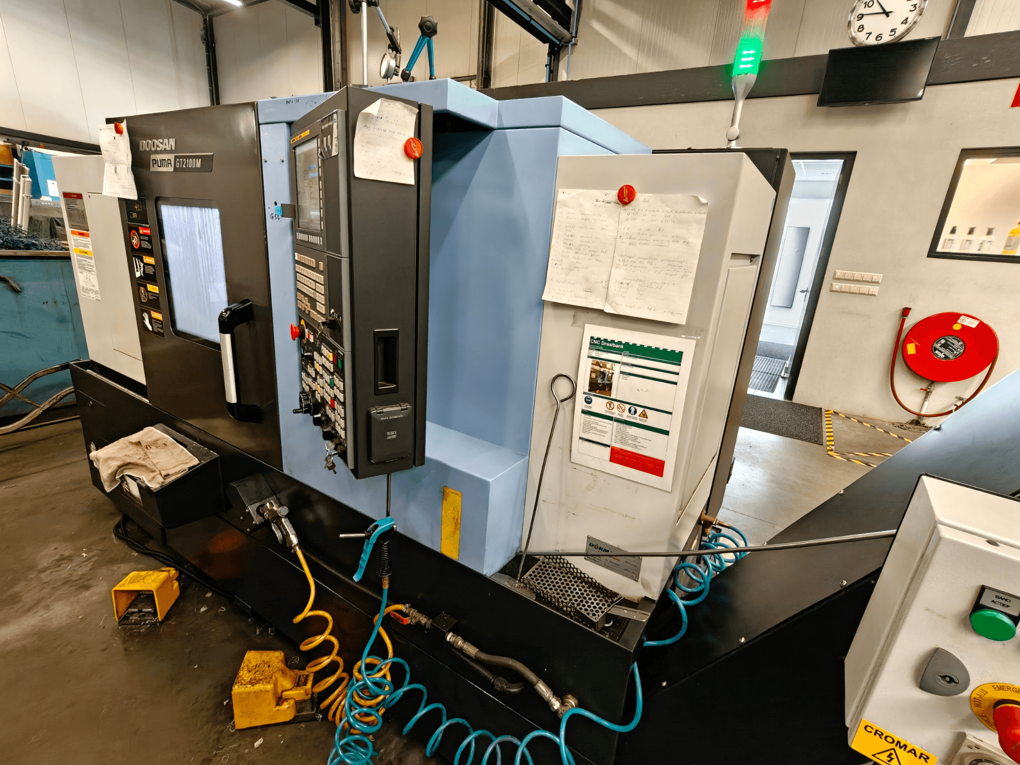 Horizontaliųjų tekinimo staklių DOOSAN Puma GT 2100M vaizdas iš priekio, matomas valdymo skydelis, saugos elementai ir techninės priežiūros pastabos.