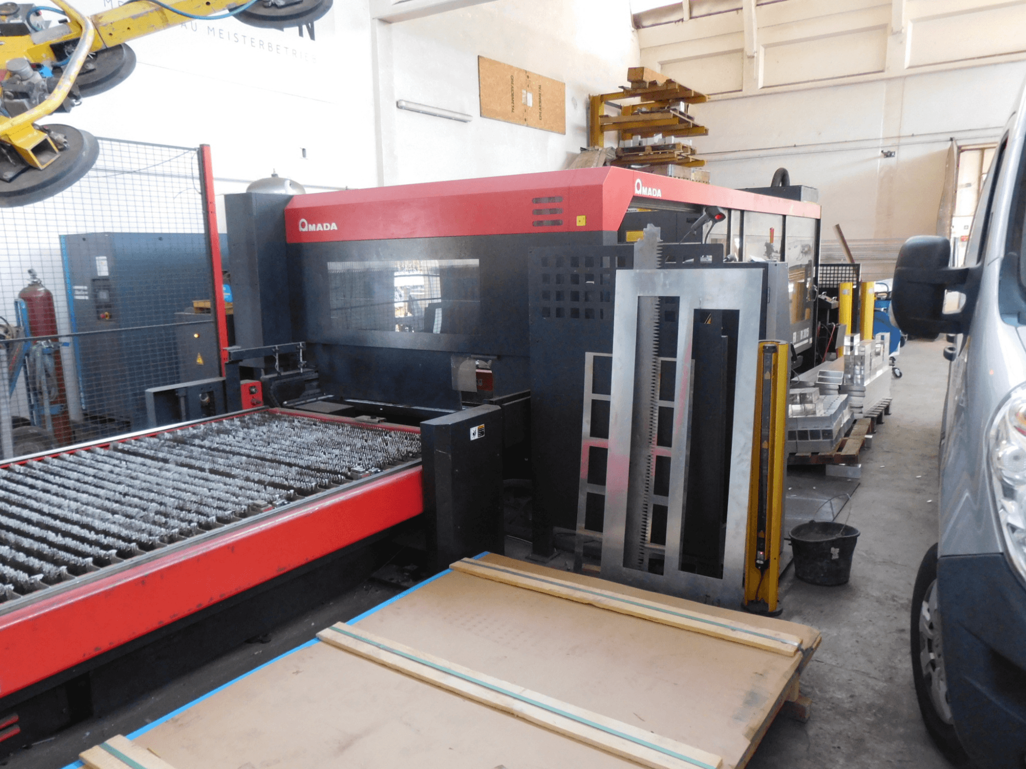 AMADA FO-3015 II RI CO2 lazerinio pjovimo staklių priekinis vaizdas su pjovimo lova ir aplink esančia darbo zona.