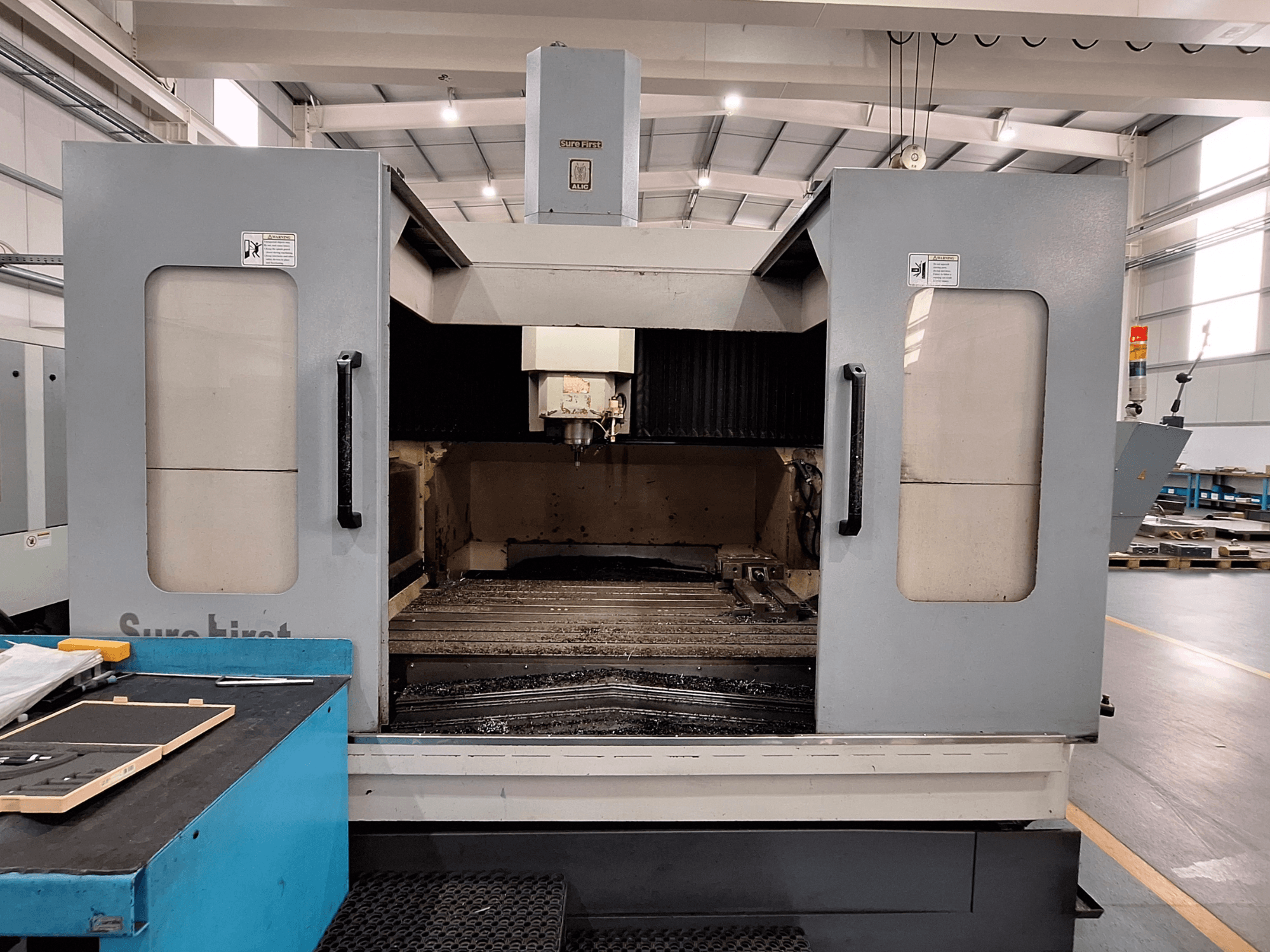 Vertikalus apdirbimo centras "Sure First QM-1836", vaizdas iš priekio, rodantis įrankių galvutę ir tuščią darbo zoną, moderni pramoninė aplinka.