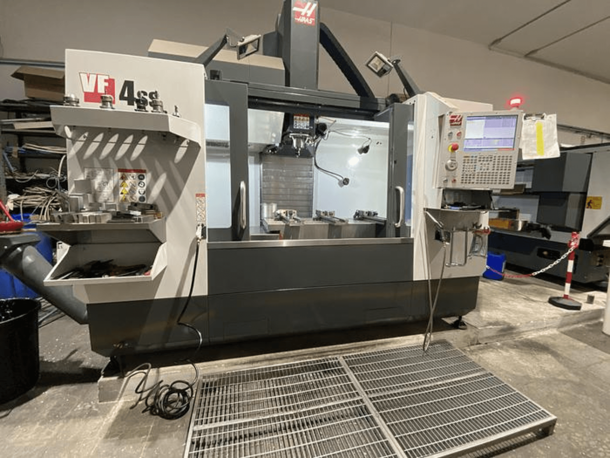 Haas VF-4SS CNC frezavimo staklės, vaizdas iš priekio, su įrankių laikymo vieta, valdymo skydeliu ir matoma darbo zona dirbtuvėse.