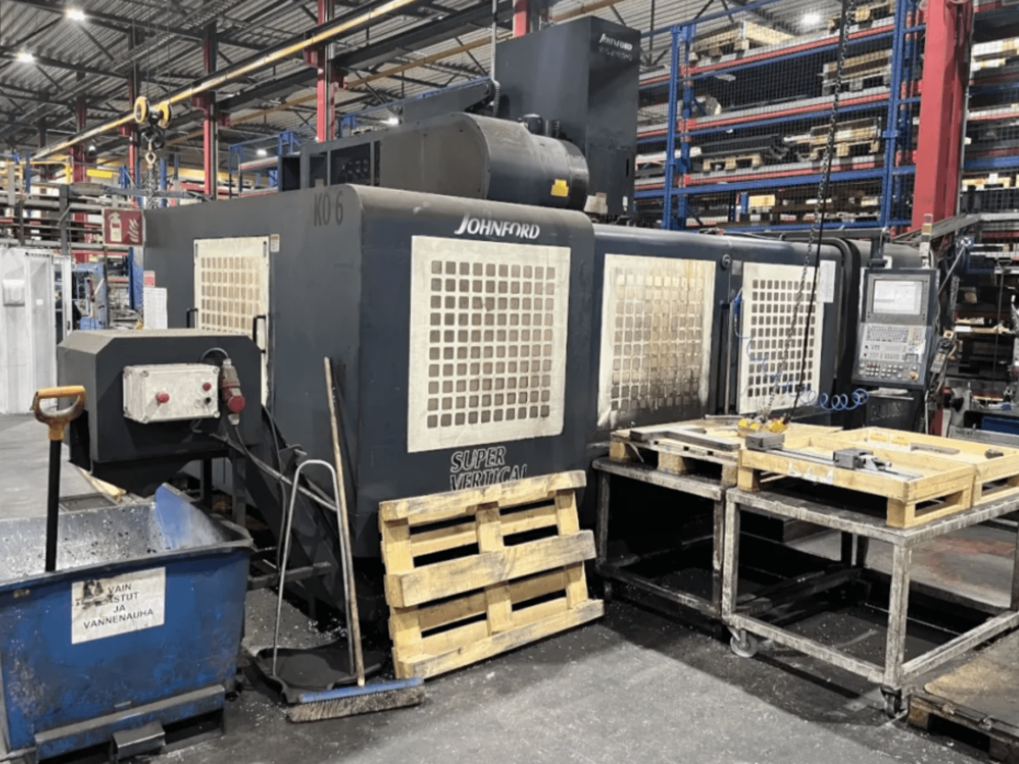 Johnford Super Vertical frezavimo staklės gamykloje, šoninis vaizdas su valdymo pultu, padėklais ir valymo įranga šalia.