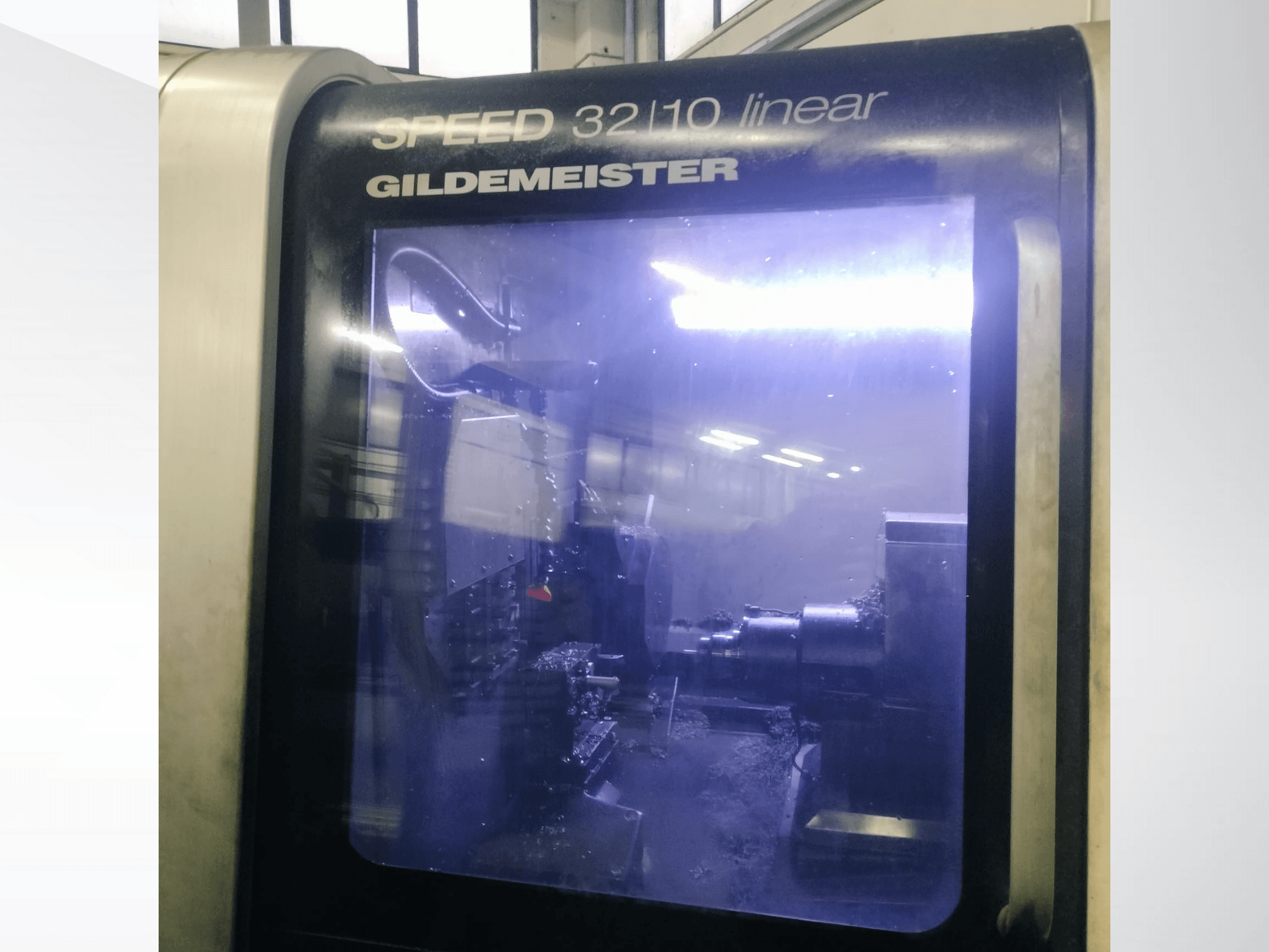 Gildemeister SPEED 3210 linijinių CNC staklių priekinis vaizdas, rodantis vidinius komponentus ir veikiantį skystą aušinimo skystį.