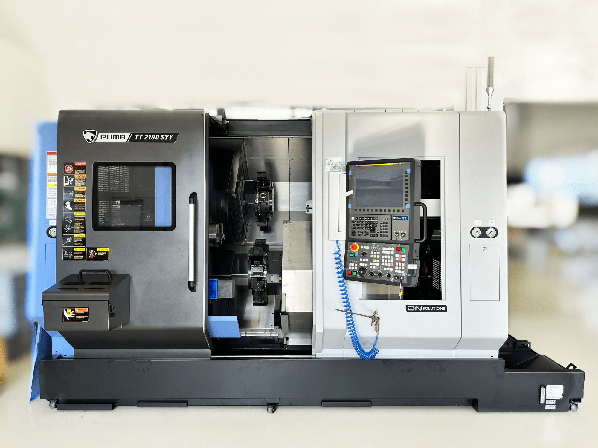 Tekinimo frezavimo centras DN SOLUTIONS PUMA TT2100SYY priekinis vaizdas su valdymo skydeliu ir matomais vidiniais komponentais.