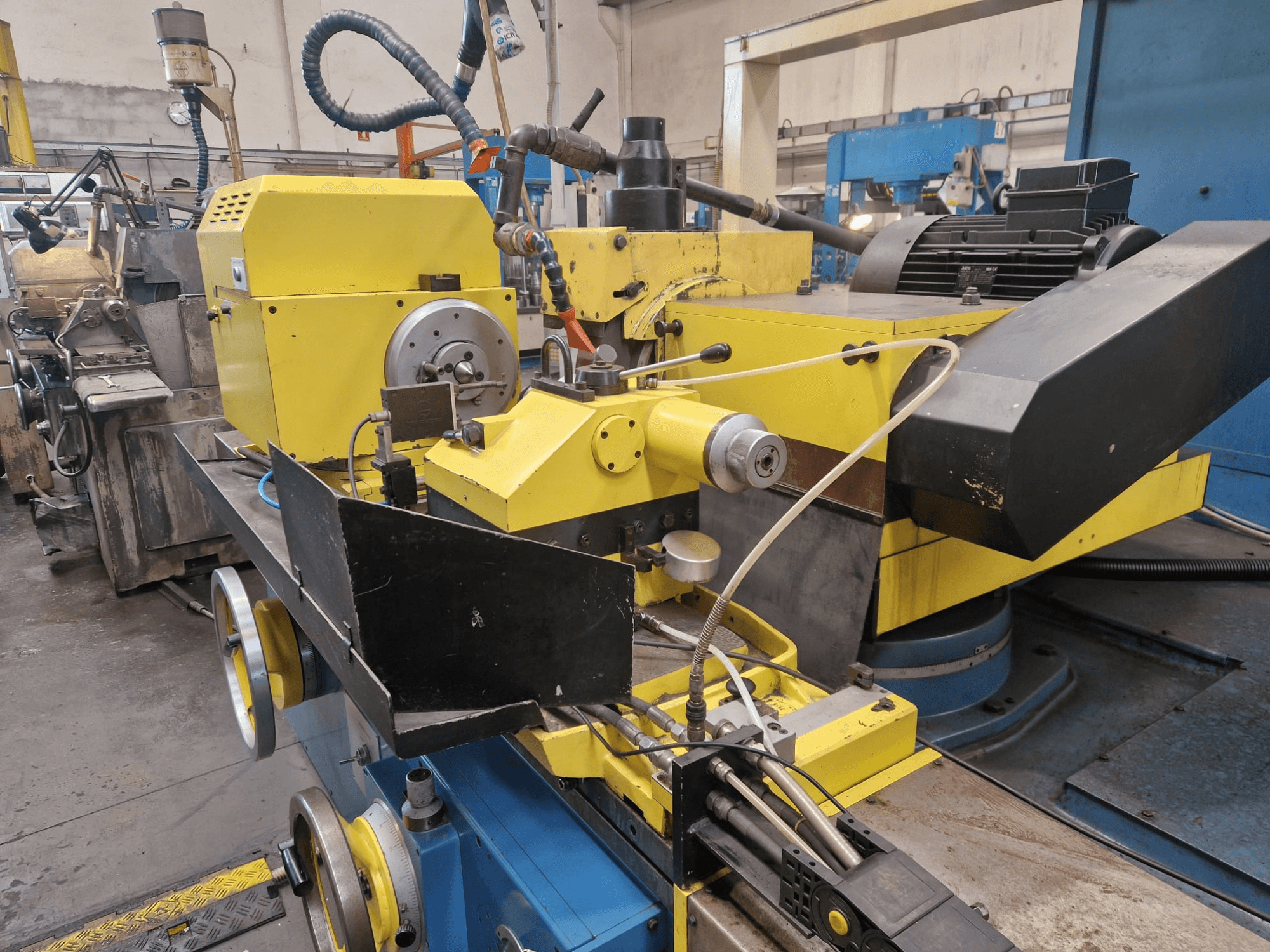 Geltonos spalvos pramoninė mašina su juoda sekcija, su ciferblatu ir žarnomis, žiūrint iš priekio nedideliu kampu.