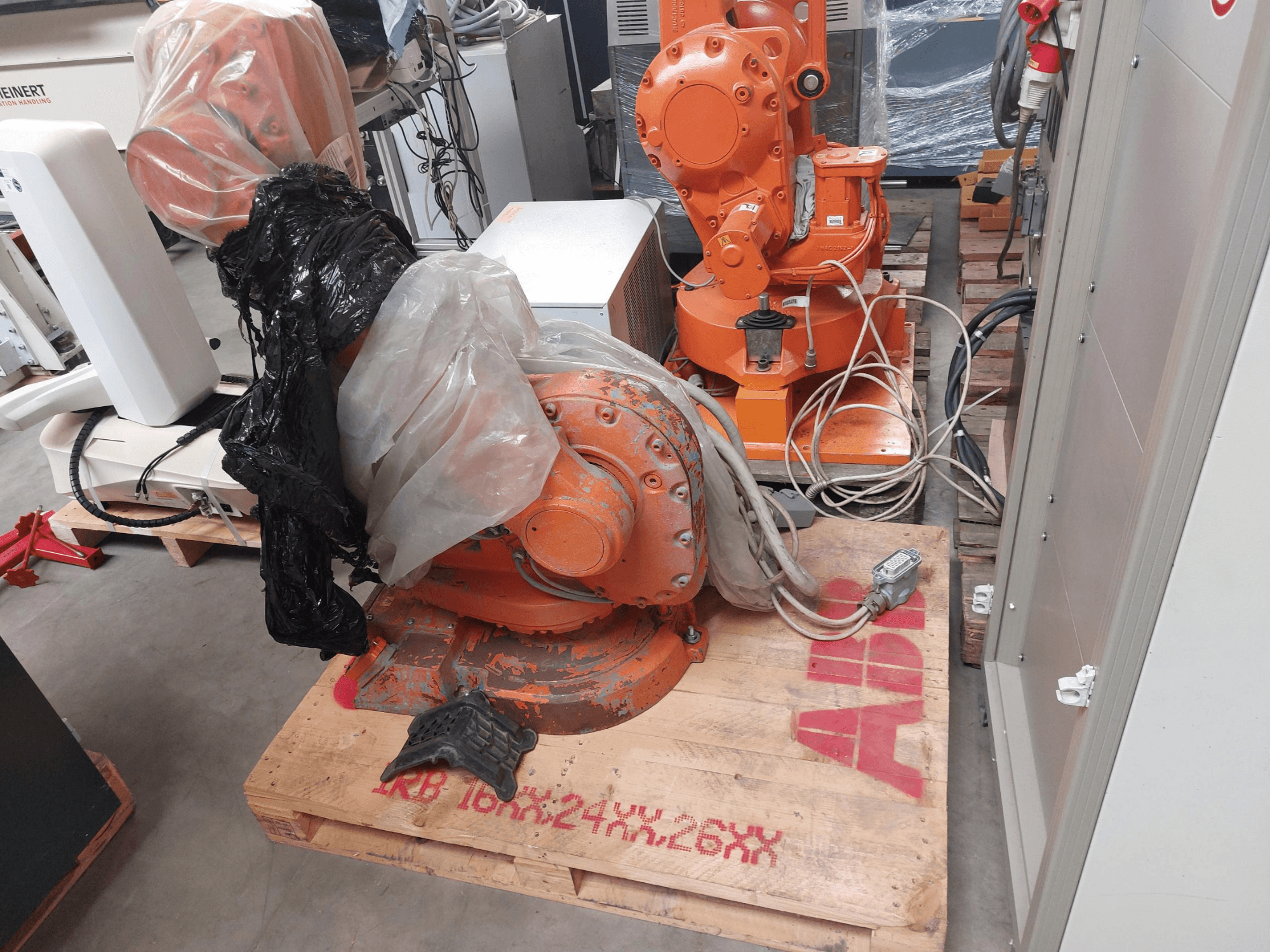 ABB IRB 1600 M2004 roboto ranka, iš dalies uždengta plastiku, žiūrint iš priekio, su šalia esančiais kabeliais ir papildomais įrenginiais.