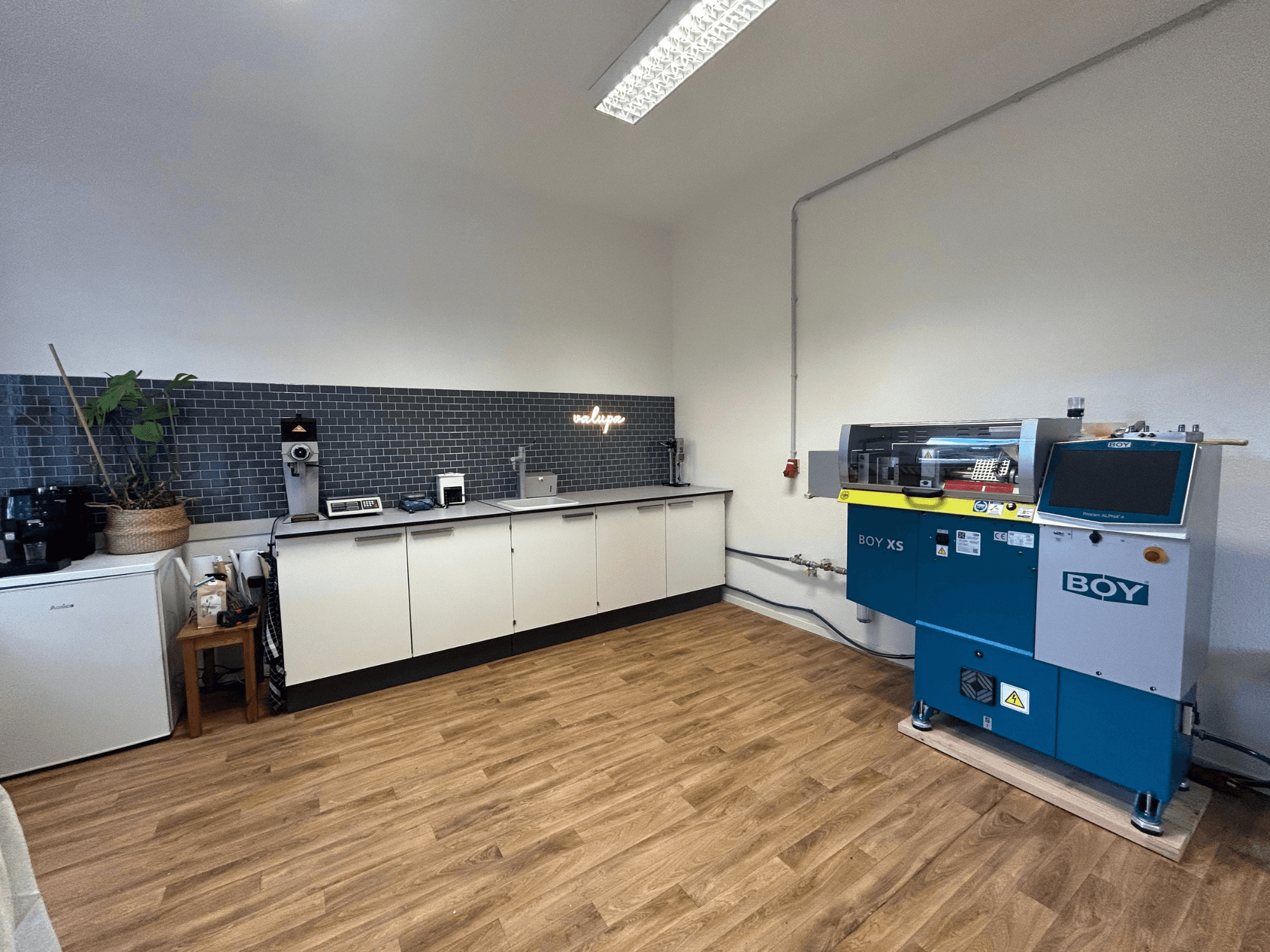 Hidraulinė liejimo mašina BOY XS 161, vaizdas iš priekio, modernioje virtuvėje su prietaisais ir medinėmis grindimis.