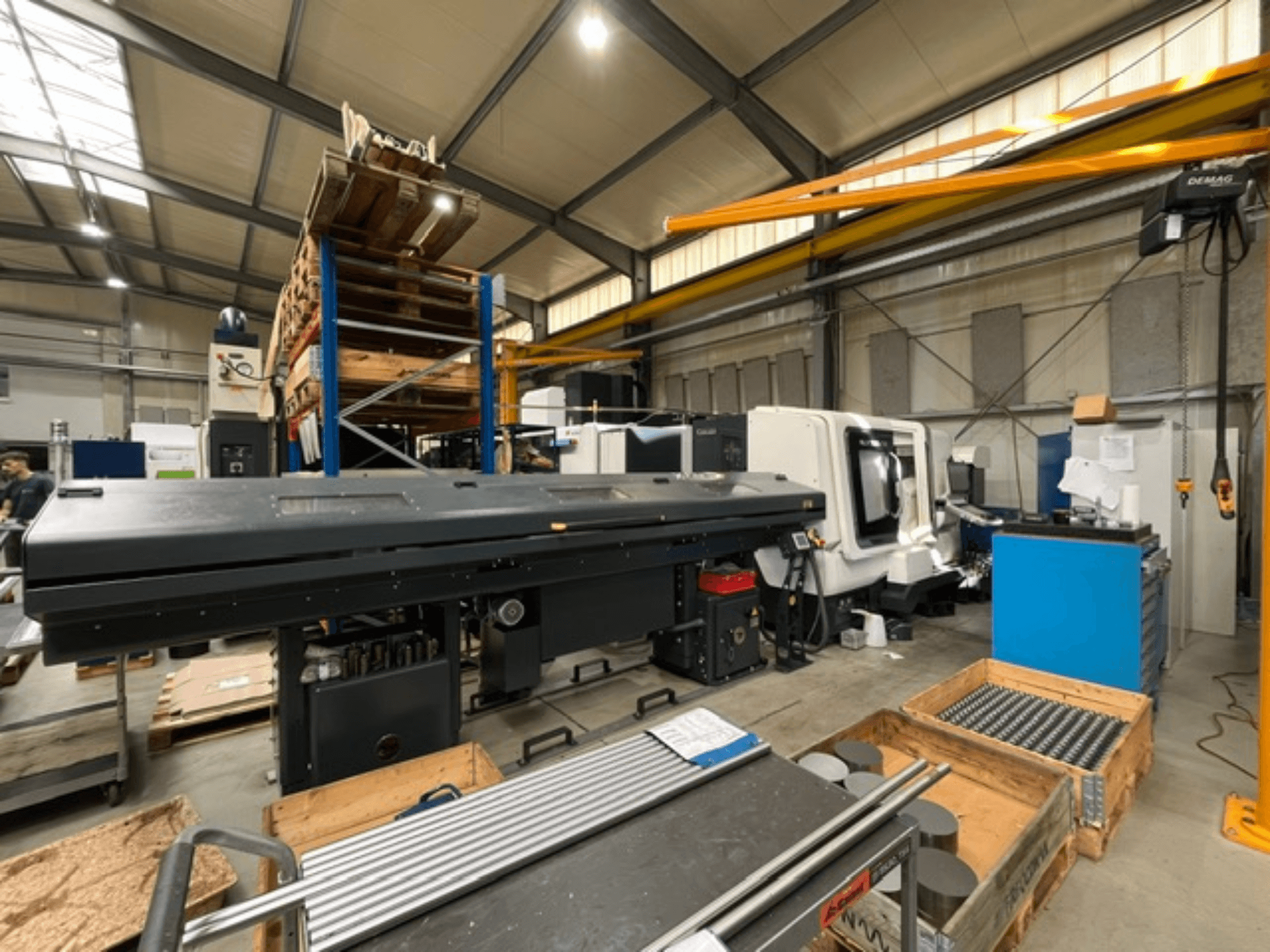 DMG MORI MORI NLX 2500/700 SY horizontalus tekinimo staklės gamyklos aplinkoje, vaizdas iš šono, matomi įrankiai ir padėklai.