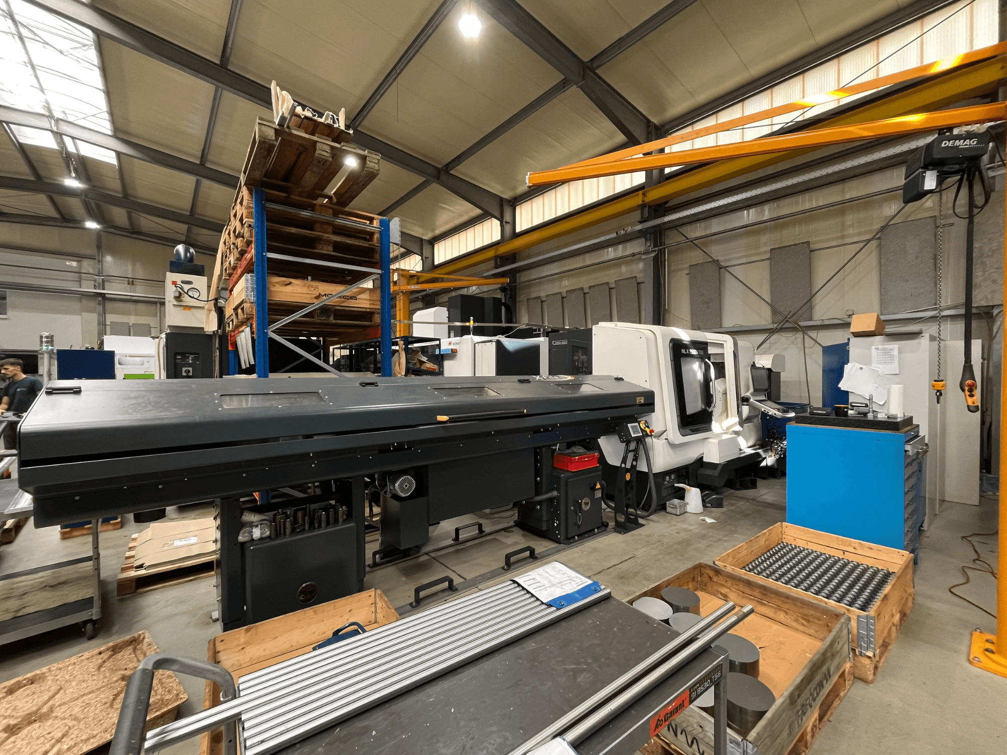 DMG MORI MORI NLX 2500/700 SY horizontalus tekinimo staklės dirbtuvėse, vaizdas iš šono, fone matomos sandėliavimo vietos ir įrankiai.