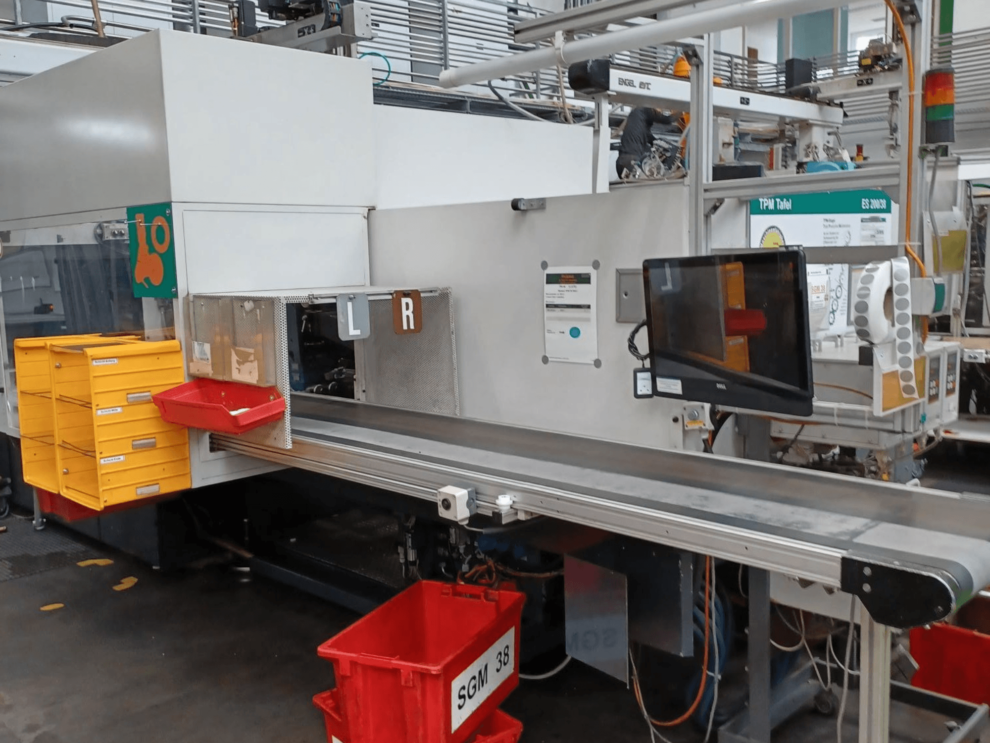 Pramoninė rūšiavimo mašina su geltonais ir raudonais konteineriais, vaizdas iš šono, su valdymo monitoriumi ir paženklintais rūšiavimo skyriais.