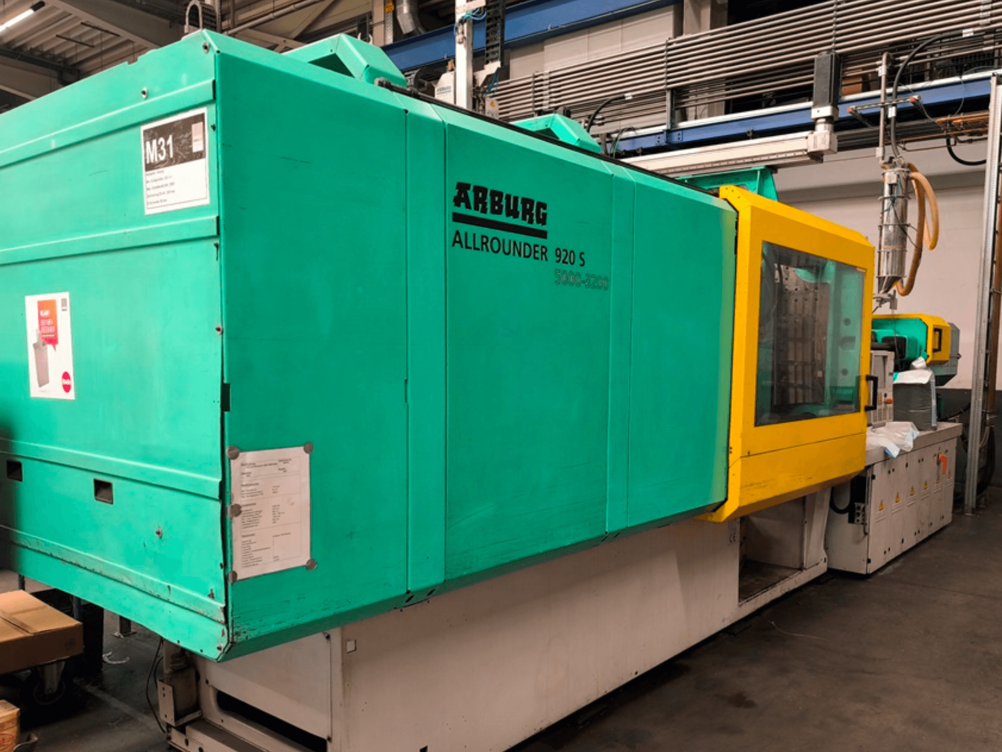 "Arburg Allrounder 920 S" vandens mėlynos ir geltonos spalvos įpurškimo liejimo mašina, šoninis vaizdas, kuriame matyti valdymo skydelis ir komponentai.