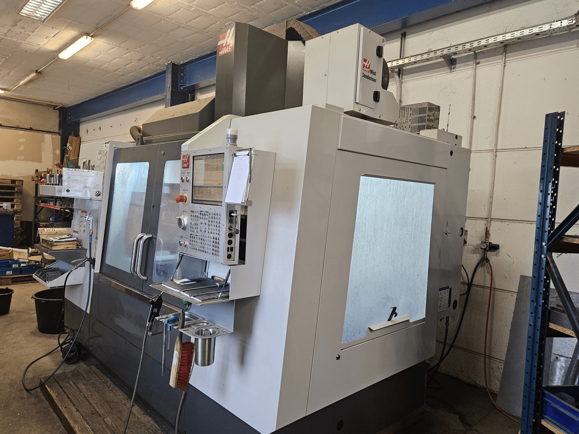 HAAS VF-4SS vertikalus apdirbimo centras, vaizdas iš priekio, su valdymo pultu ir dideliais stebėjimo langais.